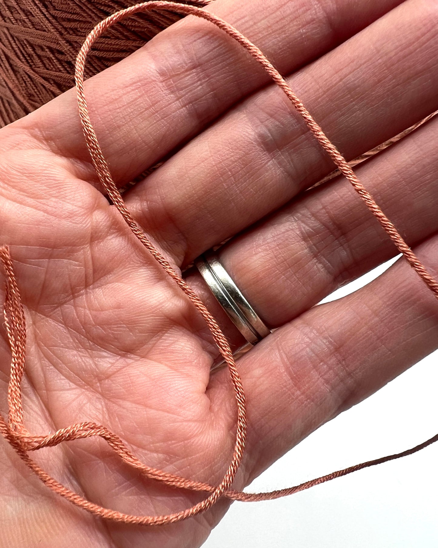 Hand holding pink thread with a silver ring on a white background