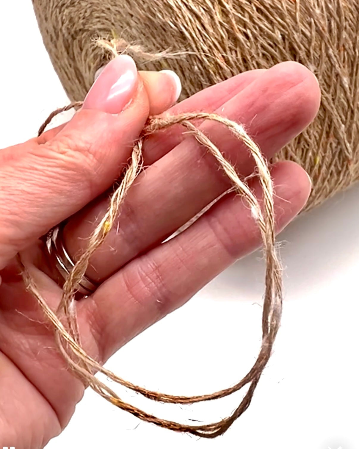 Hand holding a small loop of twine with a spool of twine in the background