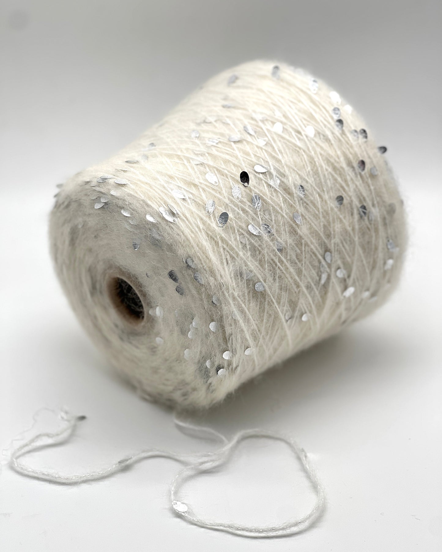 Spool of white yarn with small decorative beads on a light gray background
