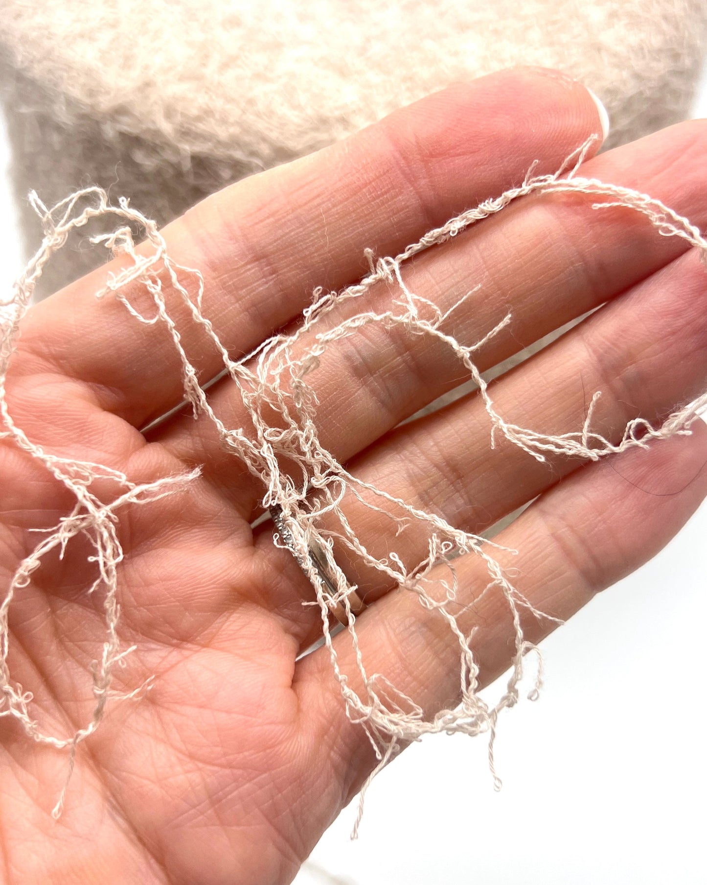 Hand holding thin, white fibers against a blurred background