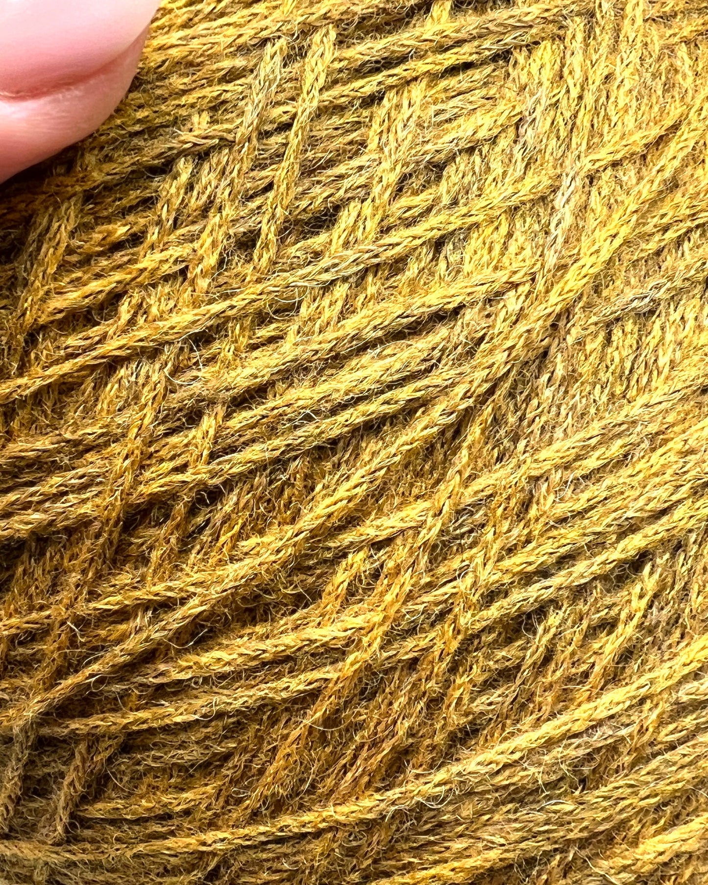 Close-up of a ball of yellow yarn with a hand for scale.