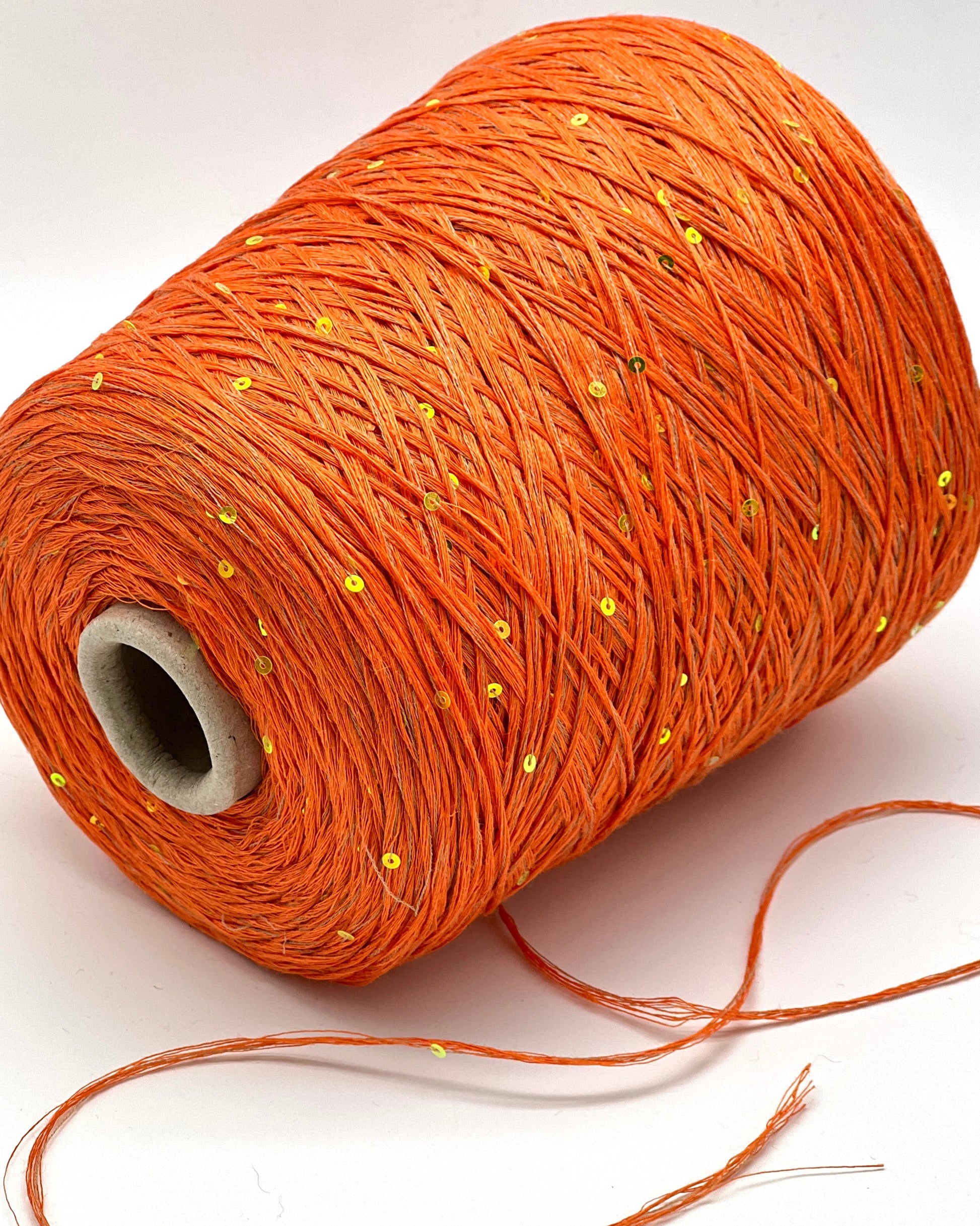 Spool of orange thread with small yellow beads on a white background