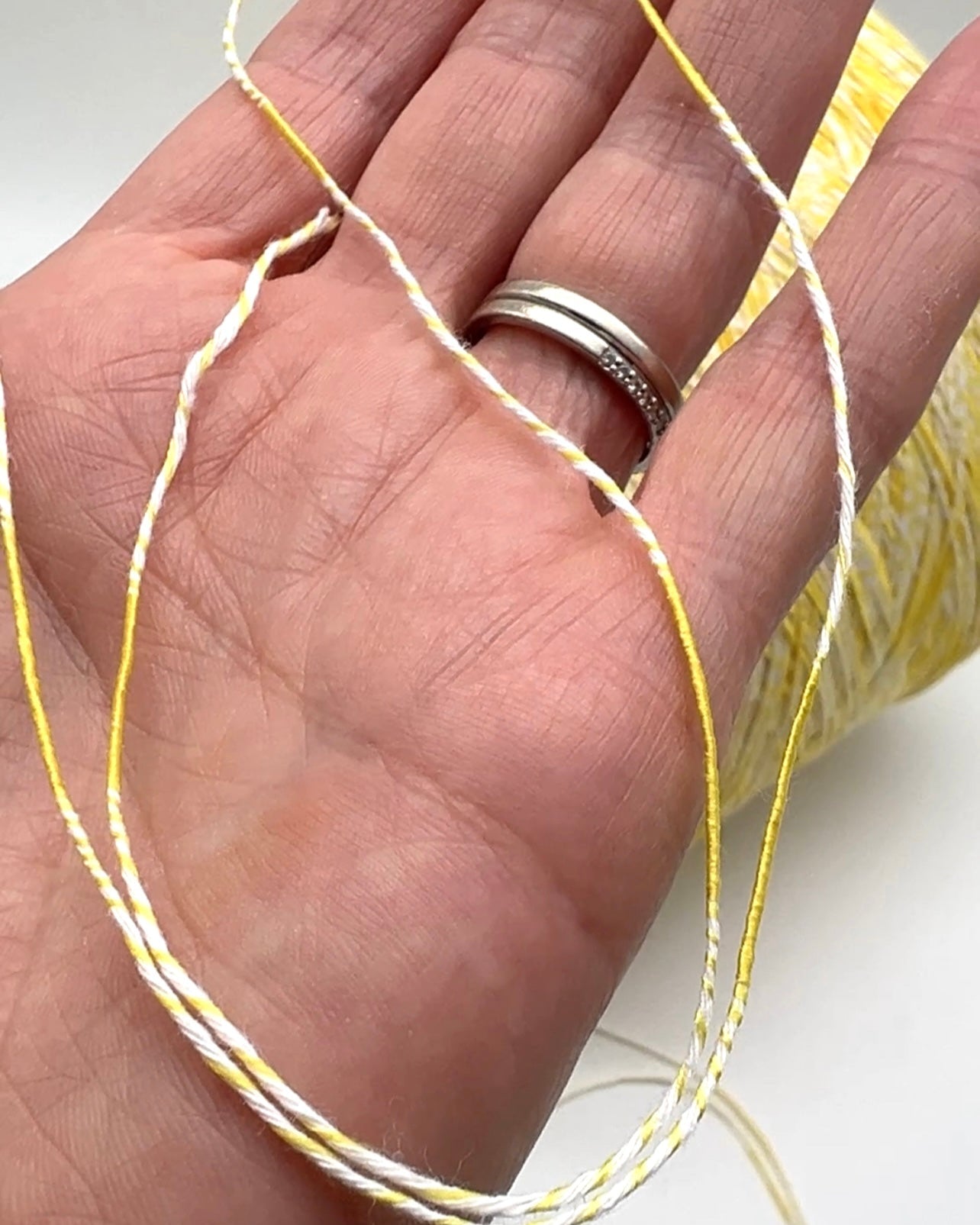 Hand holding a spool of yellow thread with a silver ring on a white background