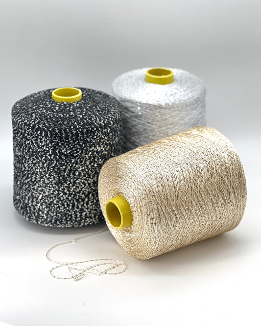 Three spools of yarn in black, white, and beige on a light gray background