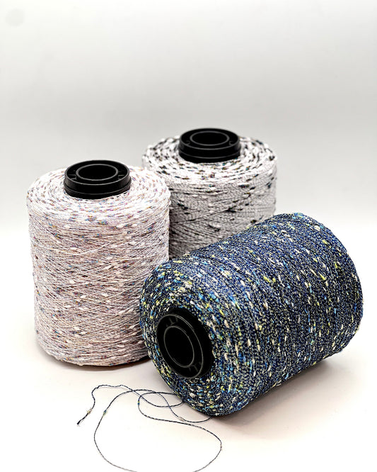Three spooRiGo Cristallo 75 percent Cotton 15 percent Lurex Italian lace weight yarn with metallic cocoons from iDOKNiTls of thread in different colors on a white background