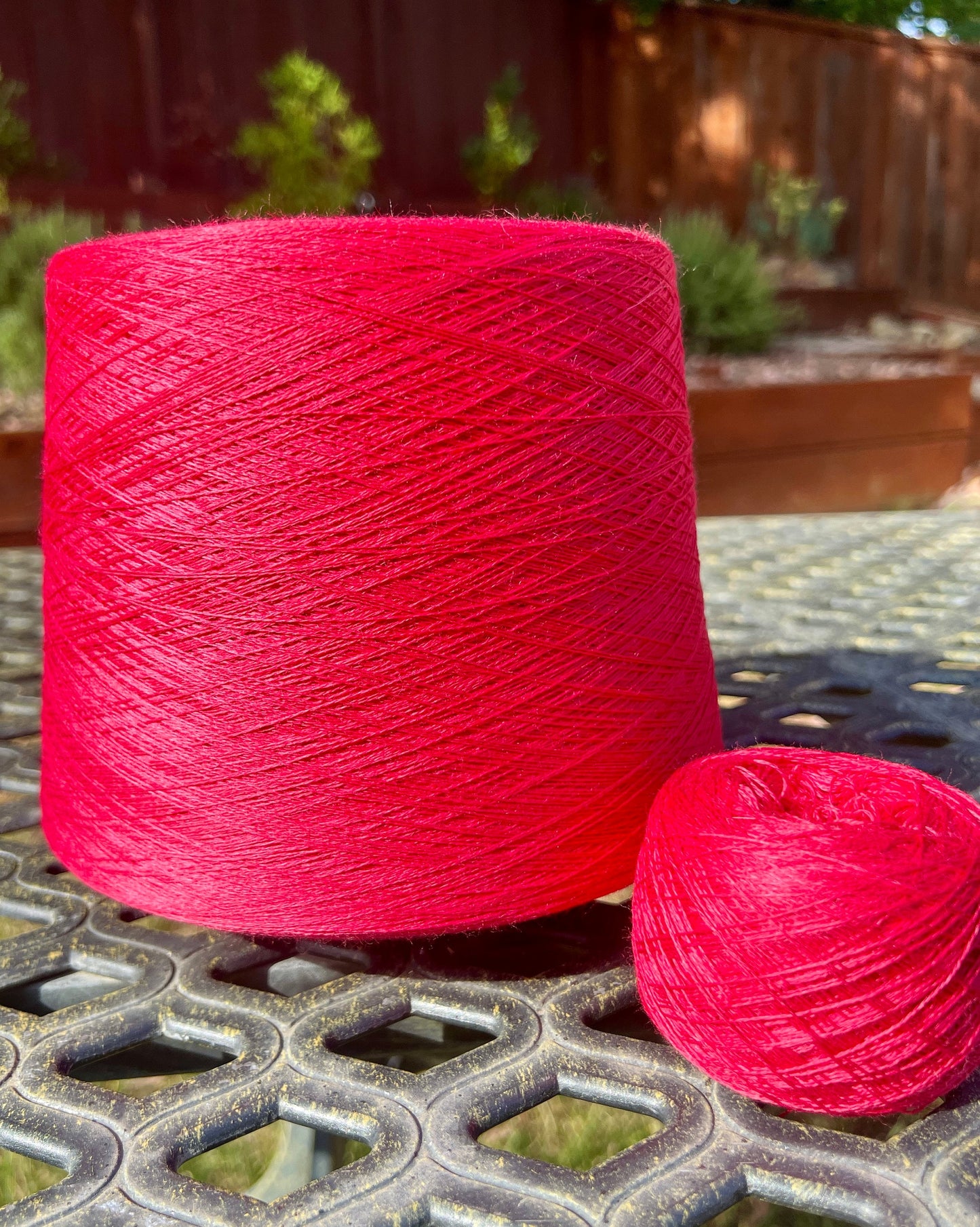 Large spool and smaller ball of red yarn on a metal surface with a garden background