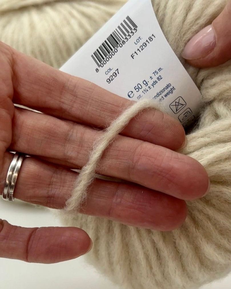Close-up of beige yarn with a label held by a hand on a white background