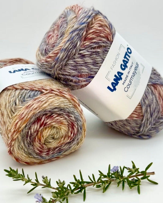 Two skeins of multicolored yarn with a label on a white background, accompanied by a sprig of rosemary.