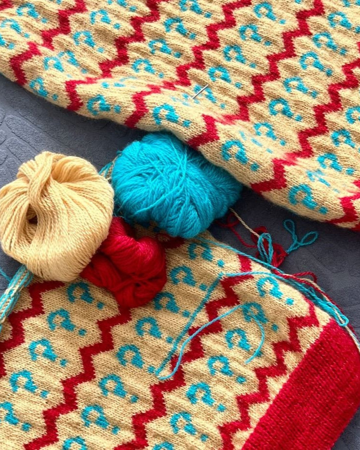 Knitted fabric with red, blue, and beige patterned yarn on a dark surface