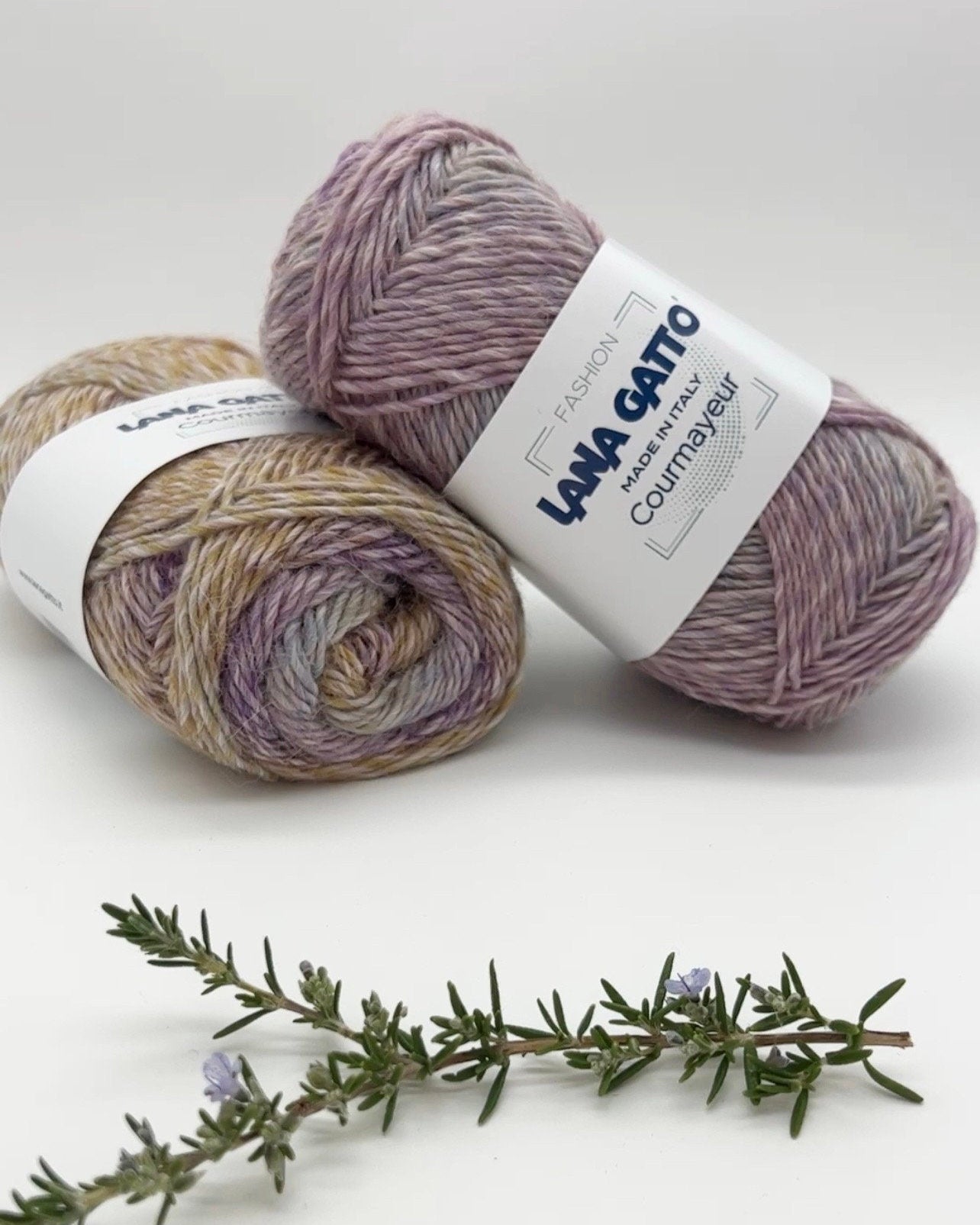 Two skeins of yarn with labels on a white background, accompanied by a sprig of rosemary.