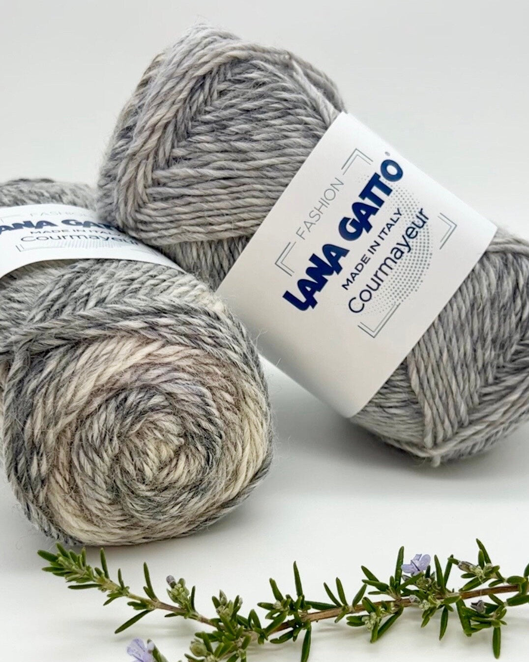 Two balls of gray yarn with a Lana Grossa label on a white background with a sprig of rosemary.