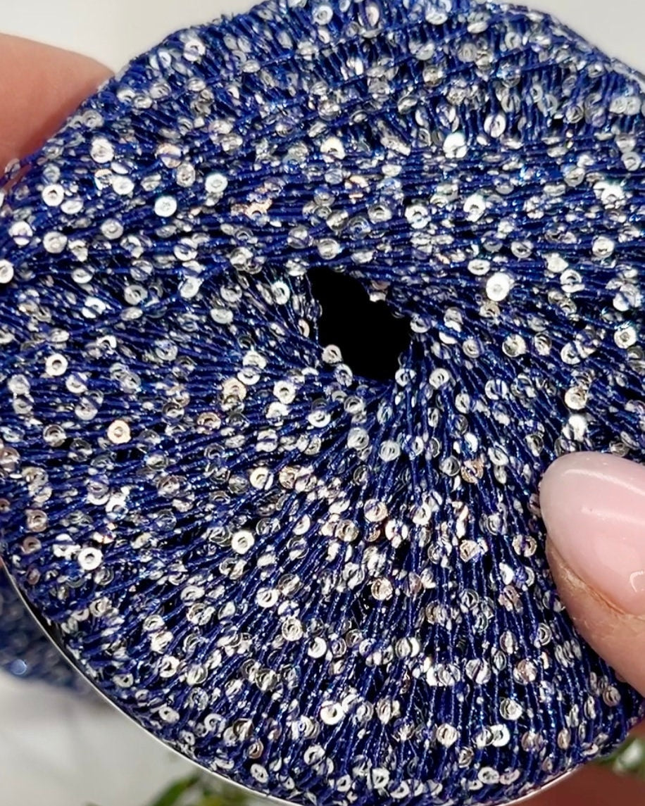 Blue scrunchie with silver sequins held by a hand against a blurred background