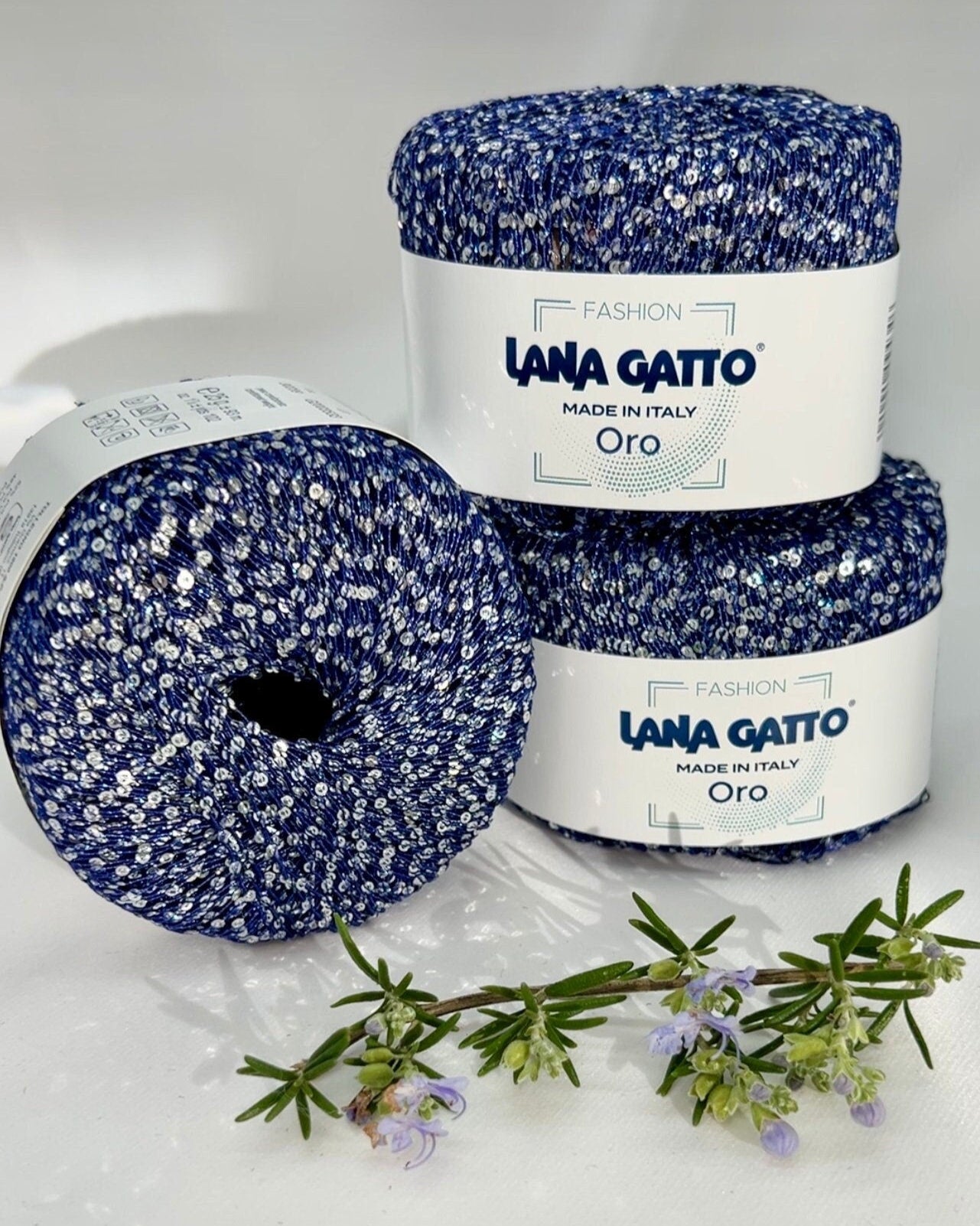 Two balls of blue yarn with white speckles and a jar labeled 'Lana Gatto' on a white background.