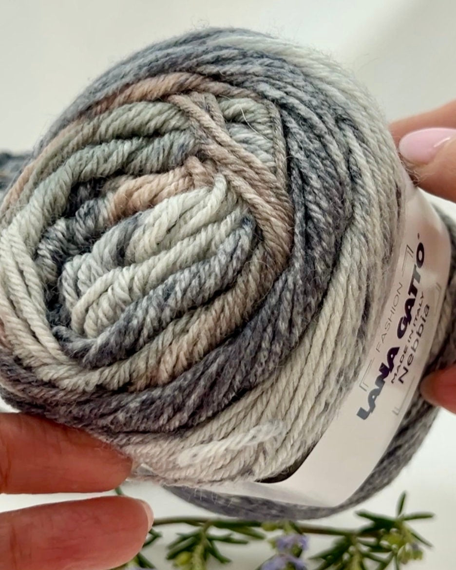 Ball of yarn with a brand label held by a hand against a light background