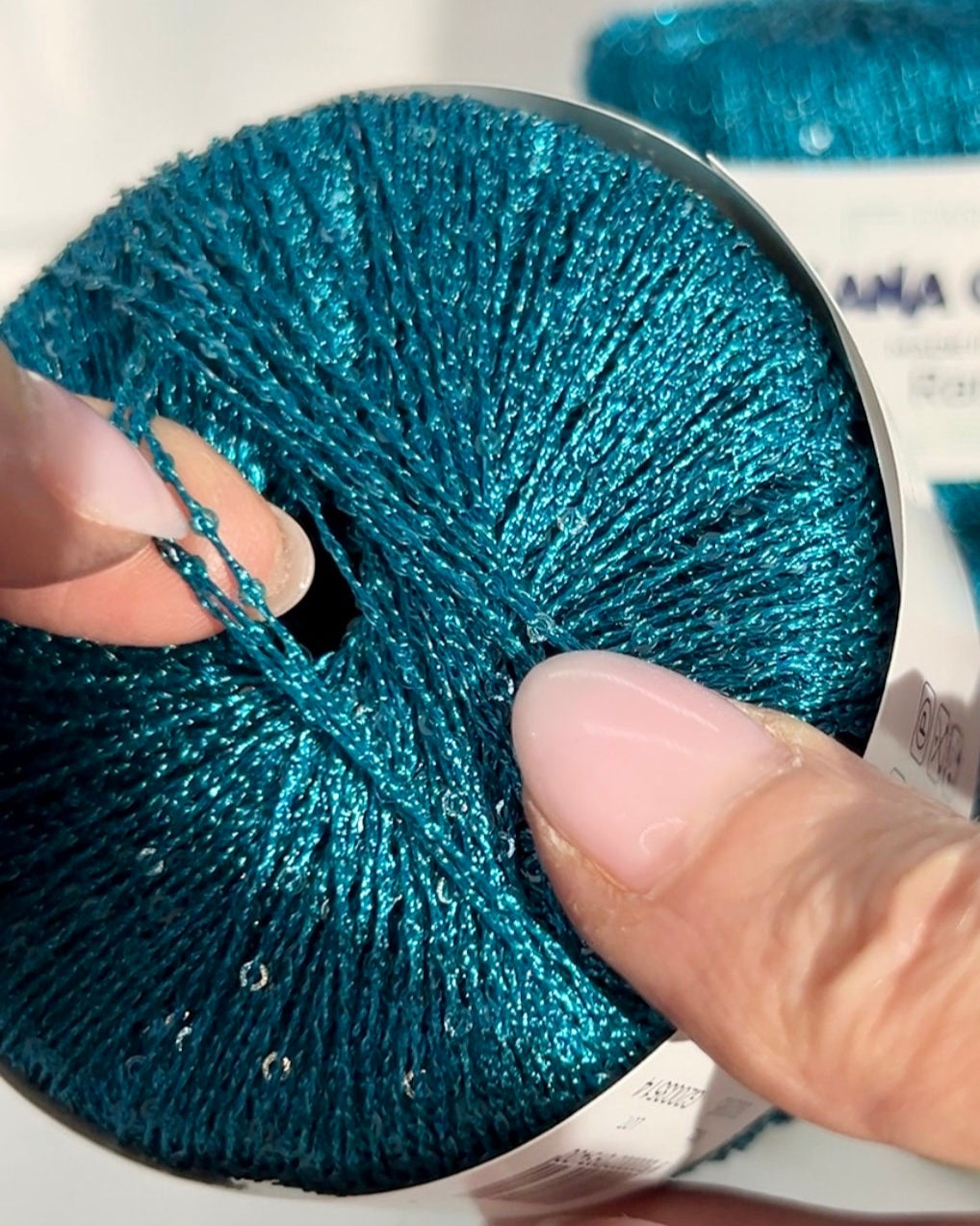 Close-up of a hand holding a blue glittery yarn ball with a white background