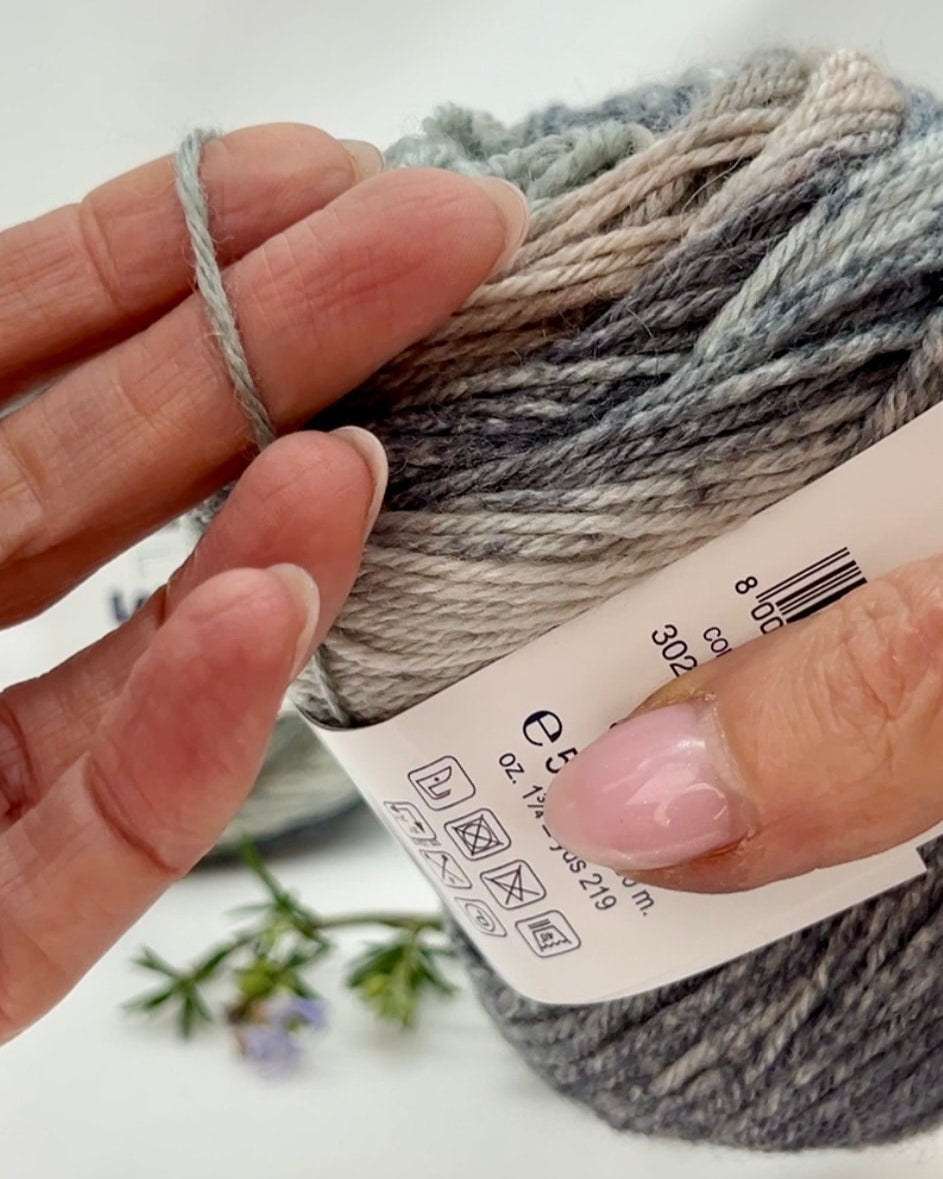 Hand holding gray yarn with a label, blurred background