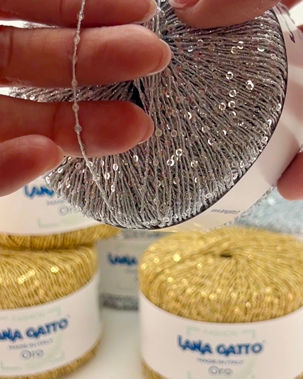 Close-up of hands holding a ball of silver yarn with gold yarn in the background.