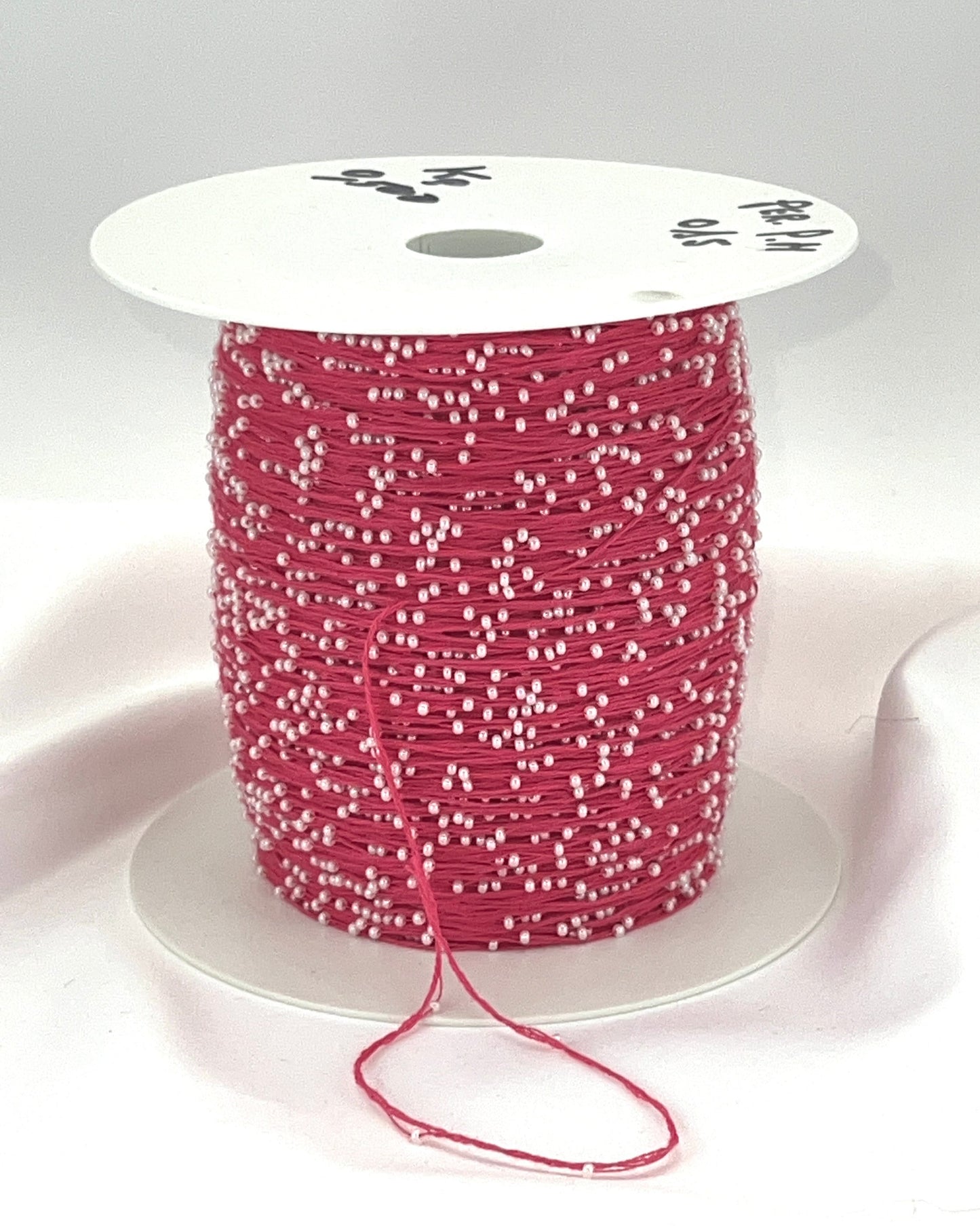 Spool of pink thread with white beads on a white background