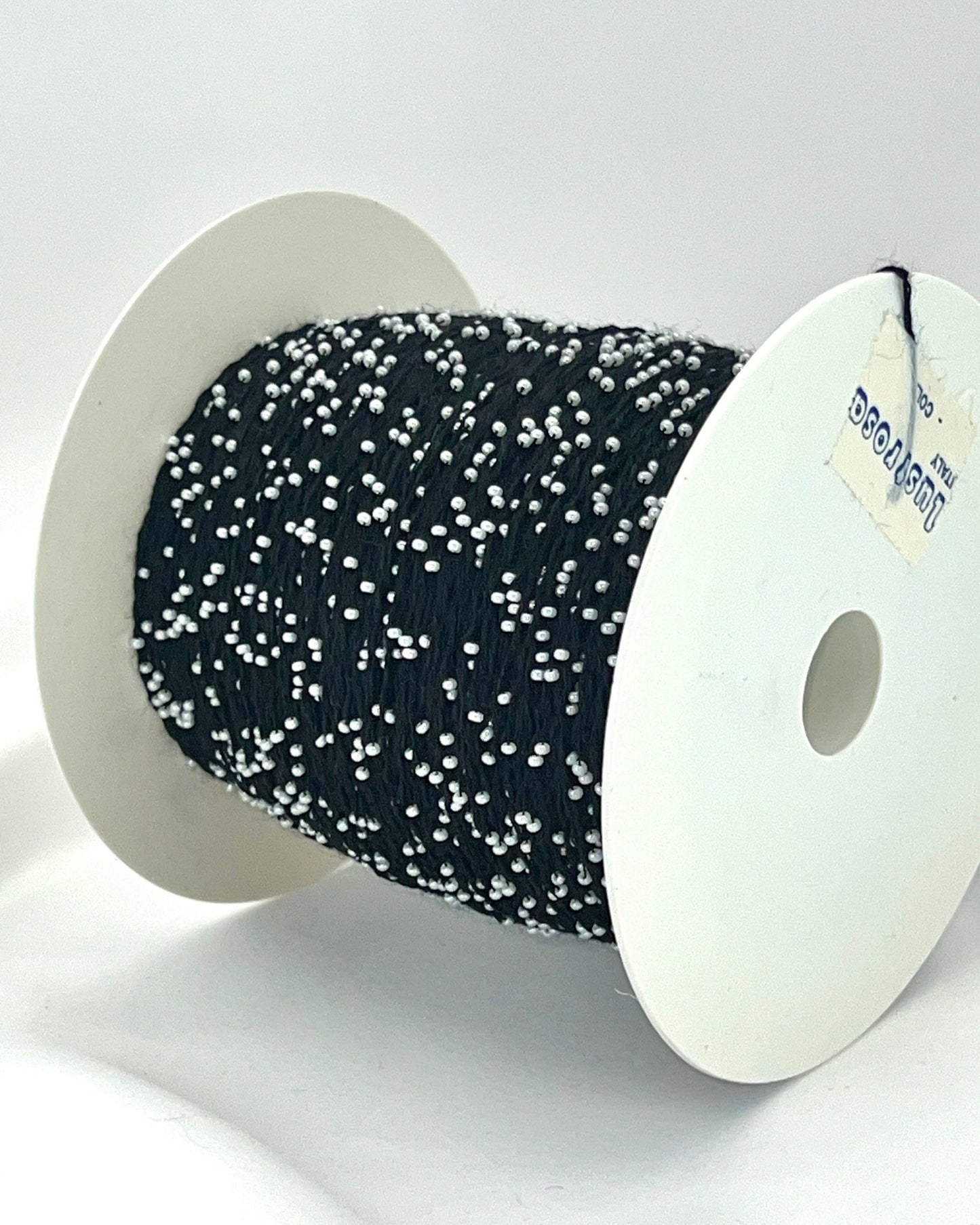 Spool of black ribbon with white specks on a white background