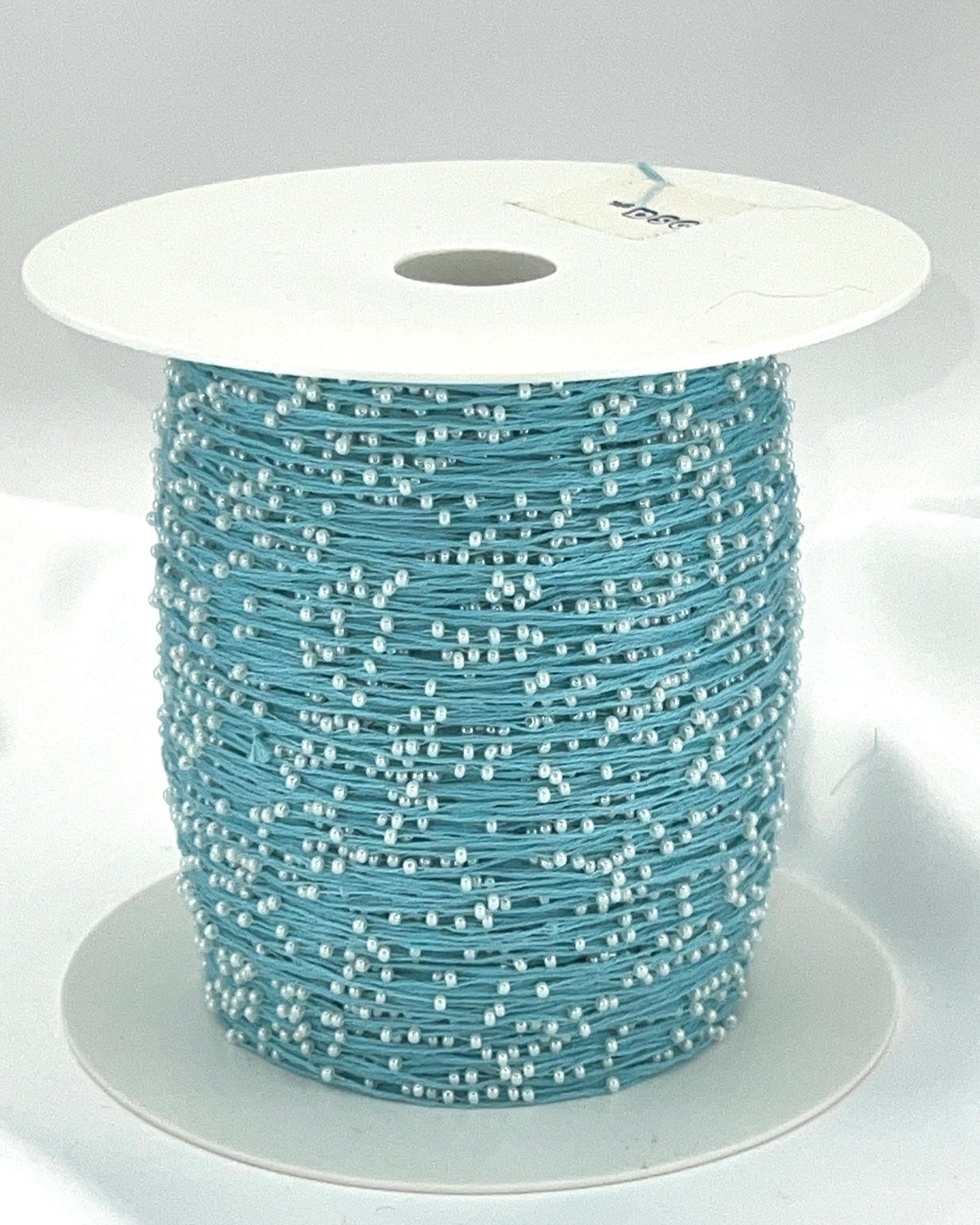 Spool of blue thread with white beads on a white background