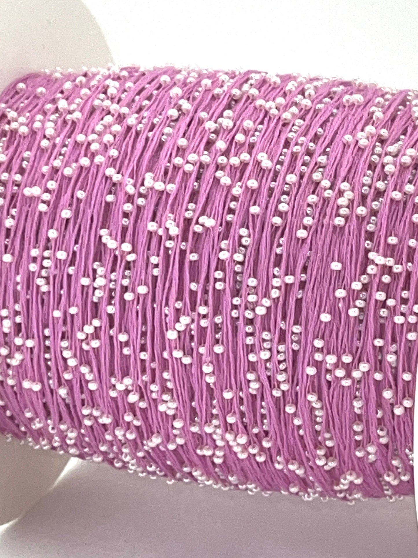 Spool of pink thread with white beads on a white background