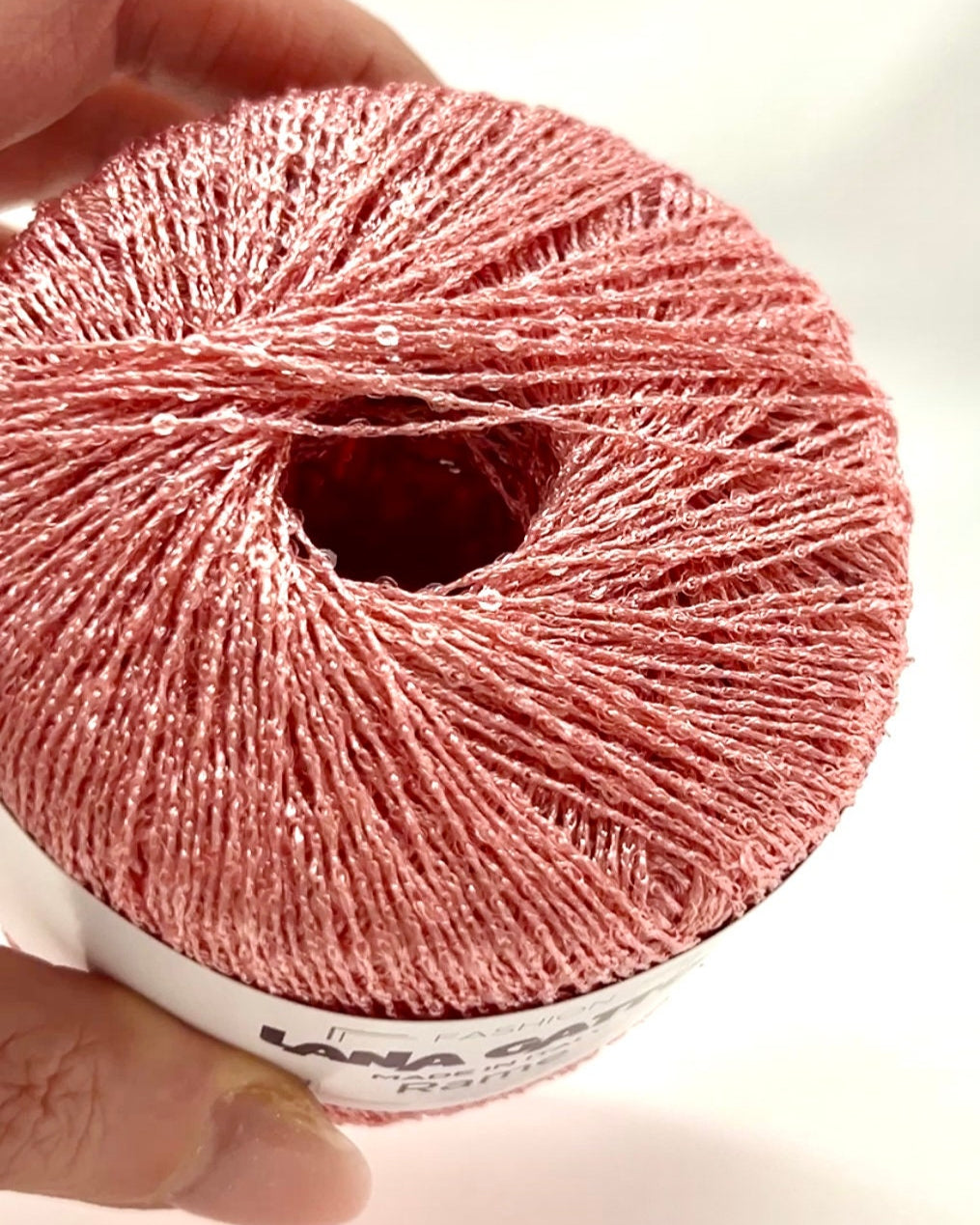 Ball of pink yarn held by a hand on a light background