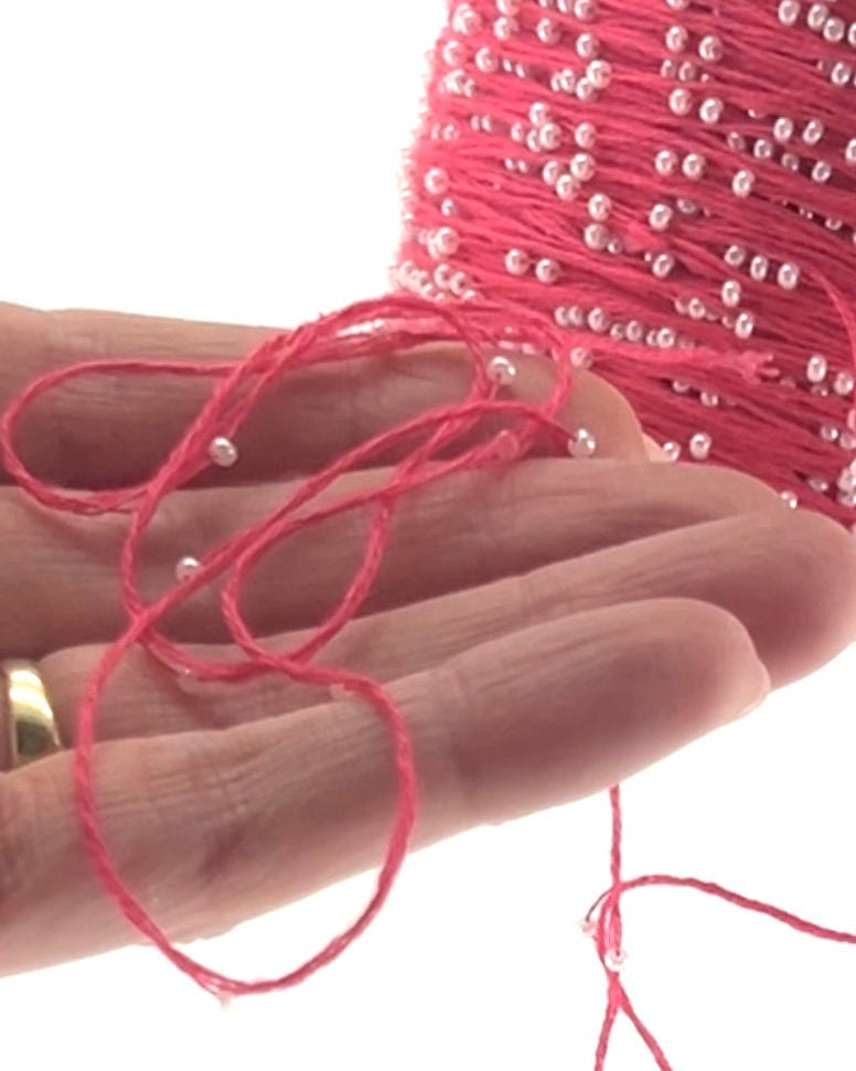 Close-up of pink beaded string held in a hand with a white background