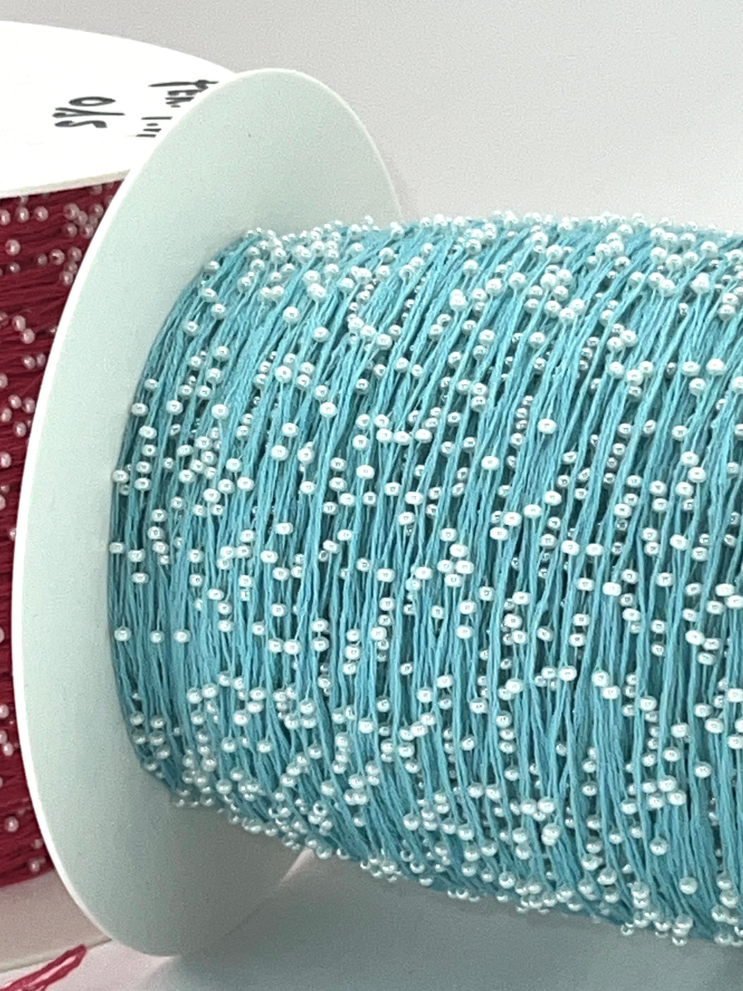 Spool of light blue thread with white beads on a white background