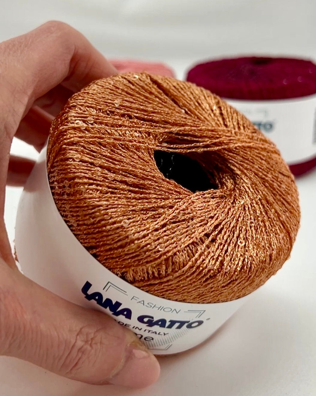 Ball of yarn with 'Lana Gatto' label held by a hand on a white background