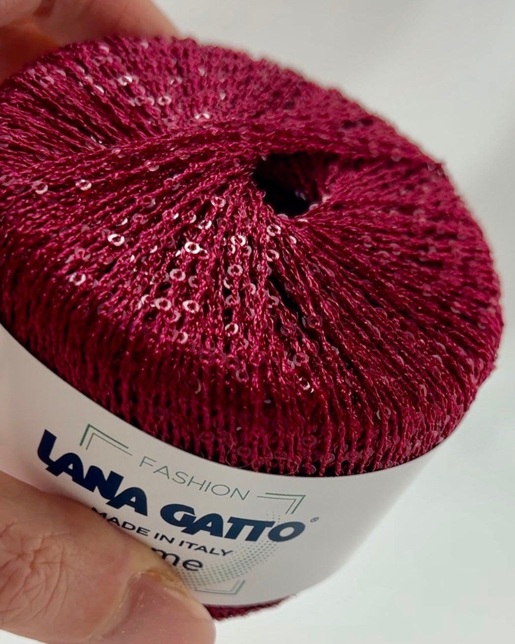 Ball of yarn with 'Lana Gatto' label held by a hand on a white background