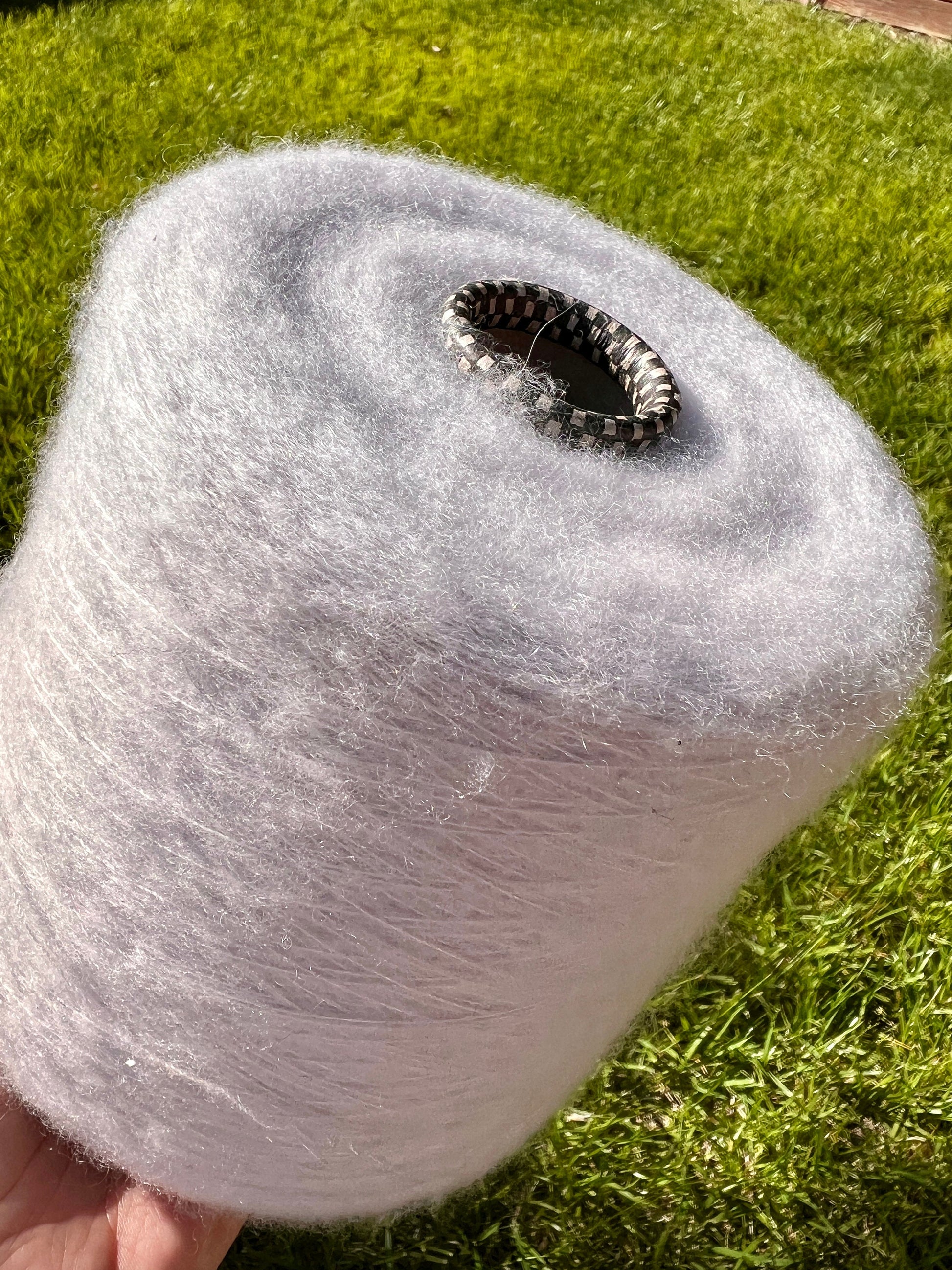 Large spool of white yarn held against a grassy background