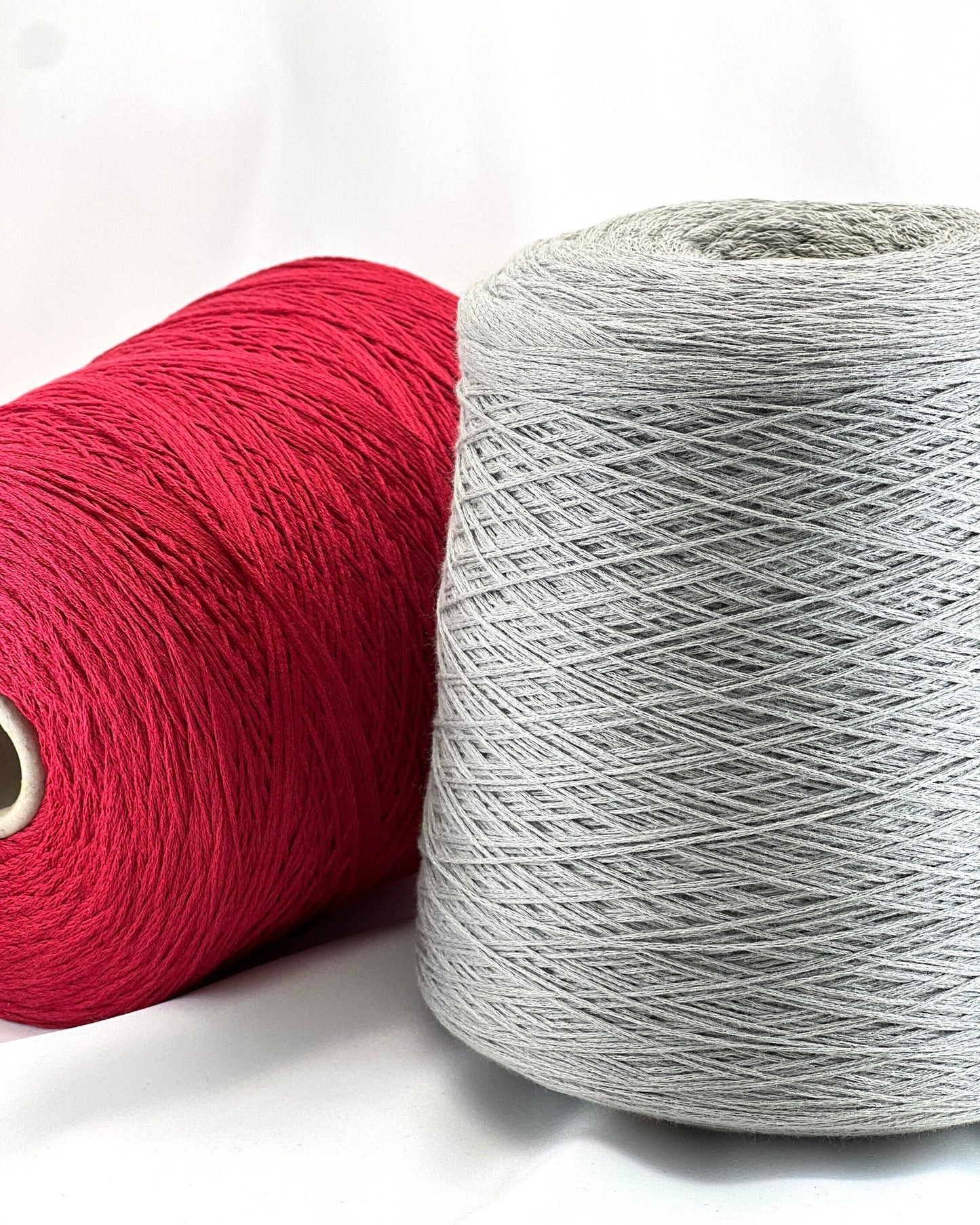 Two spools of yarn, one red and one gray, on a white background