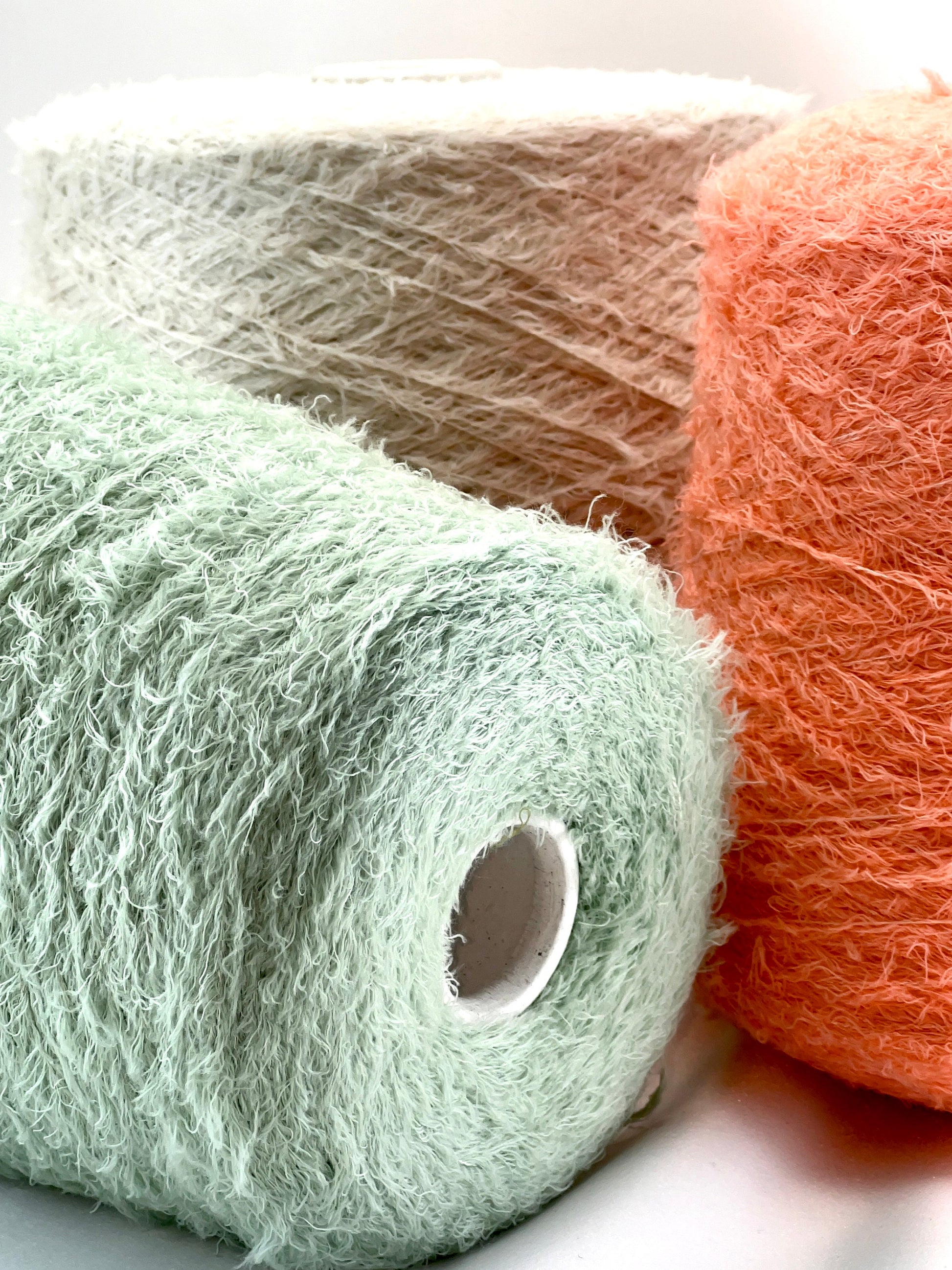 Three skeins of yarn in green, pink, and orange on a white background