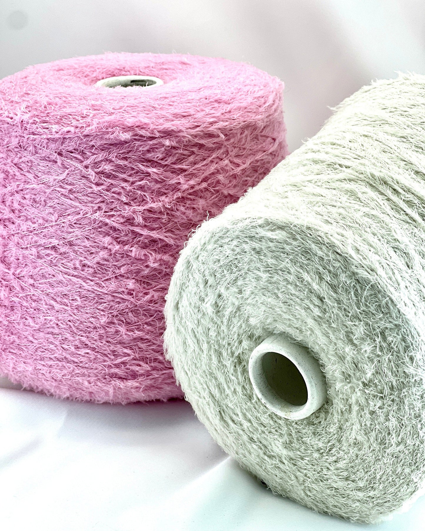 Two rolls of yarn, one pink and one white, on a light background