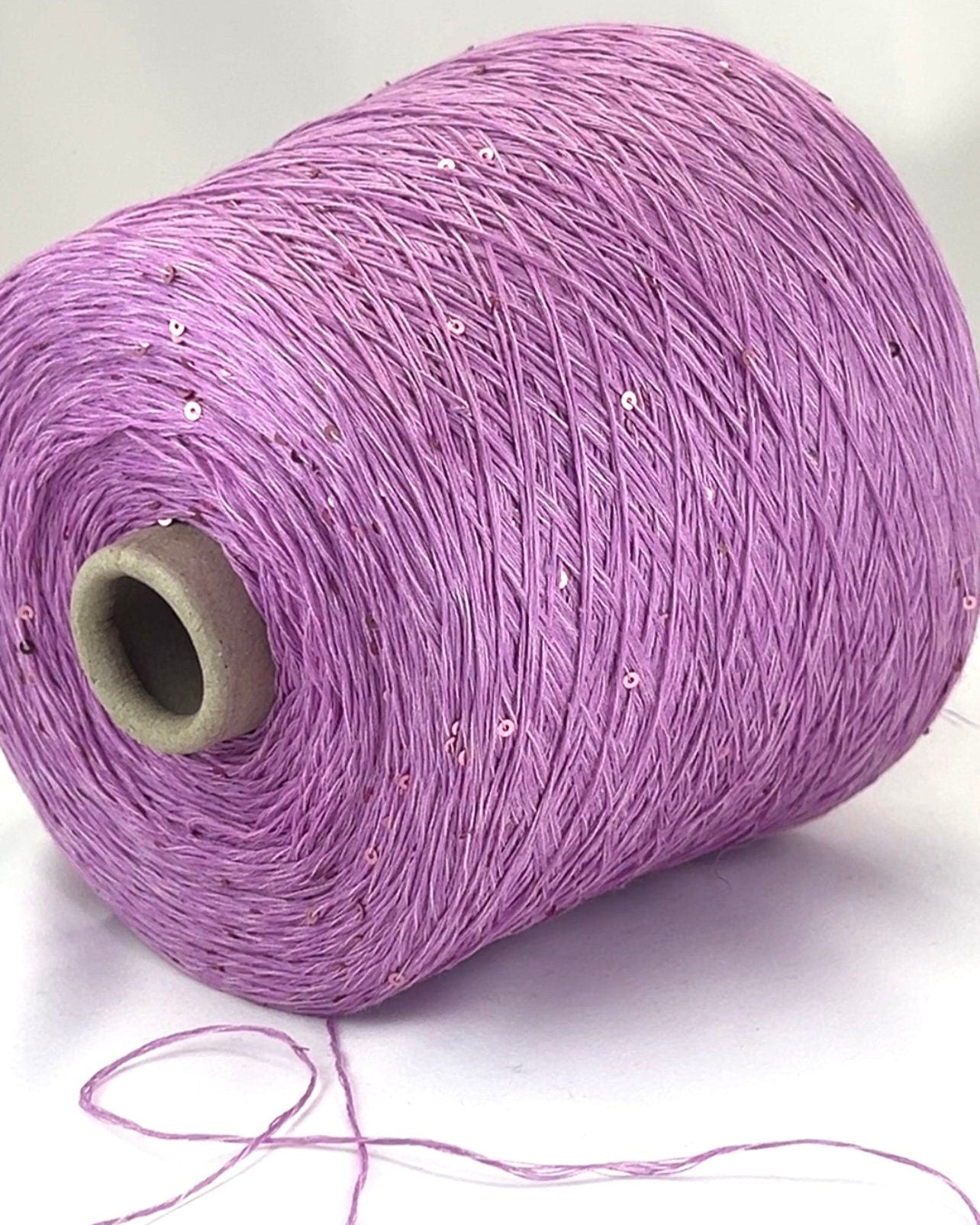 Spool of purple yarn with sequins on a white background