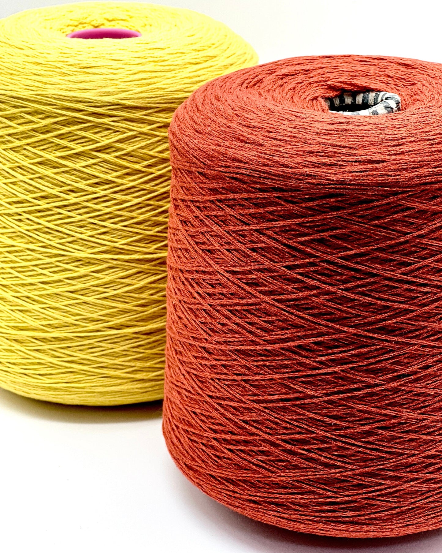 Two spools of yellow and red yarn on a white background