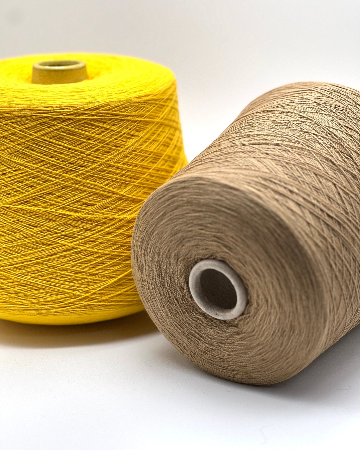 Two spools of yarn, one yellow and one beige, on a white background.