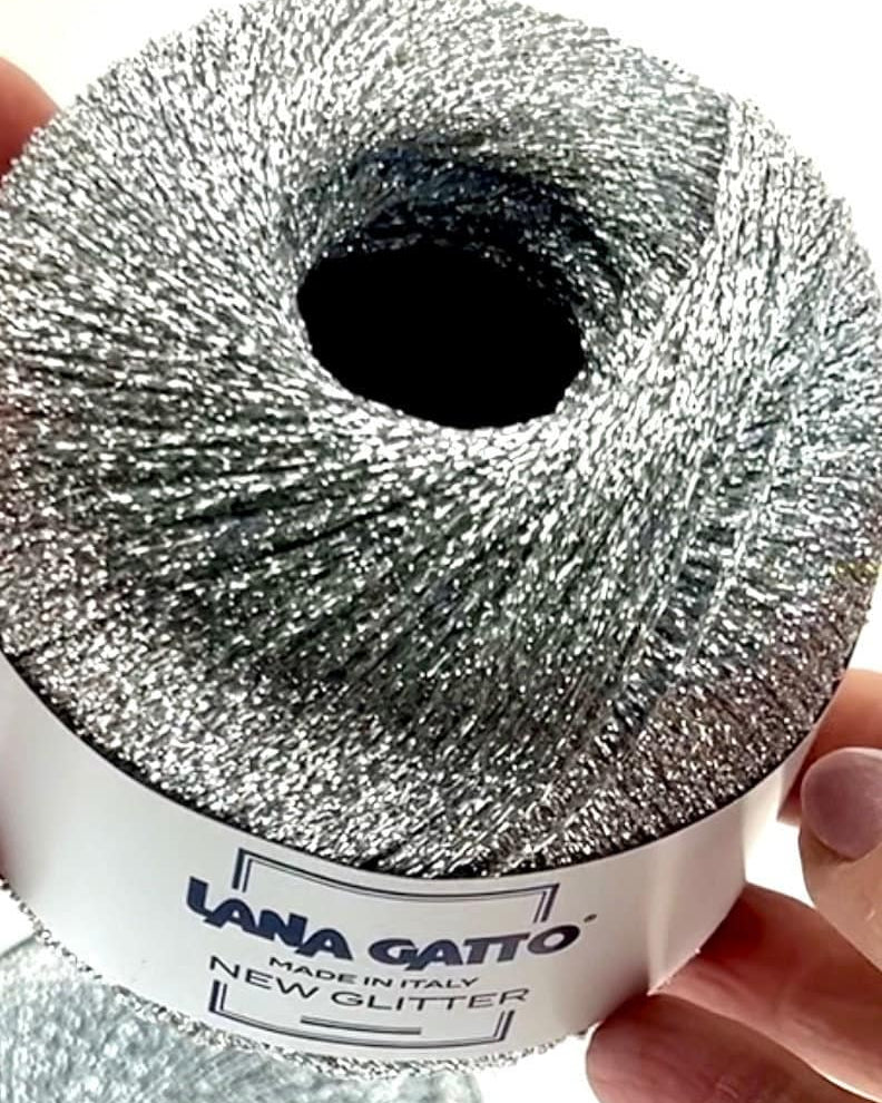 Roll of silver glitter yarn held by a hand with 'Lana Gatto' label.