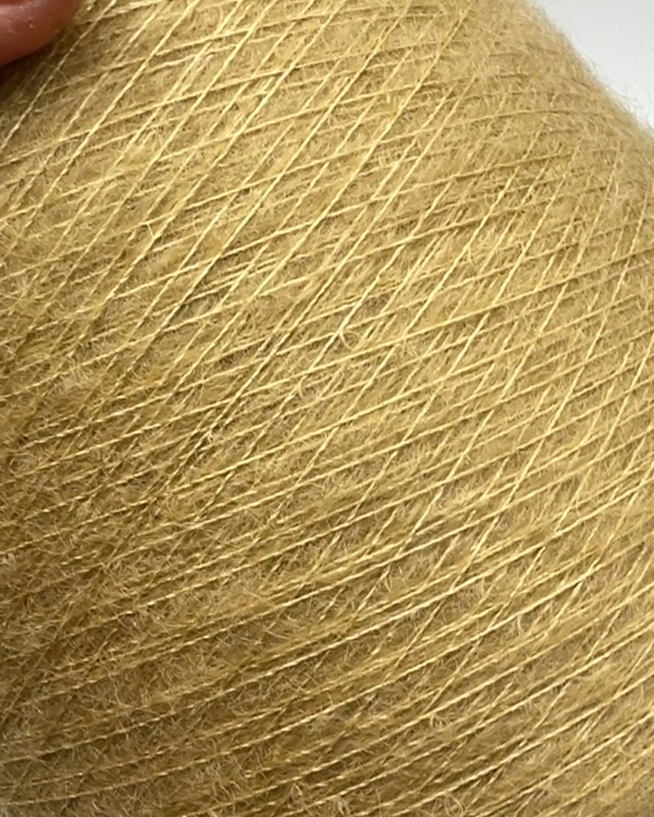 Close-up of a ball of yellow yarn with a hand holding it.