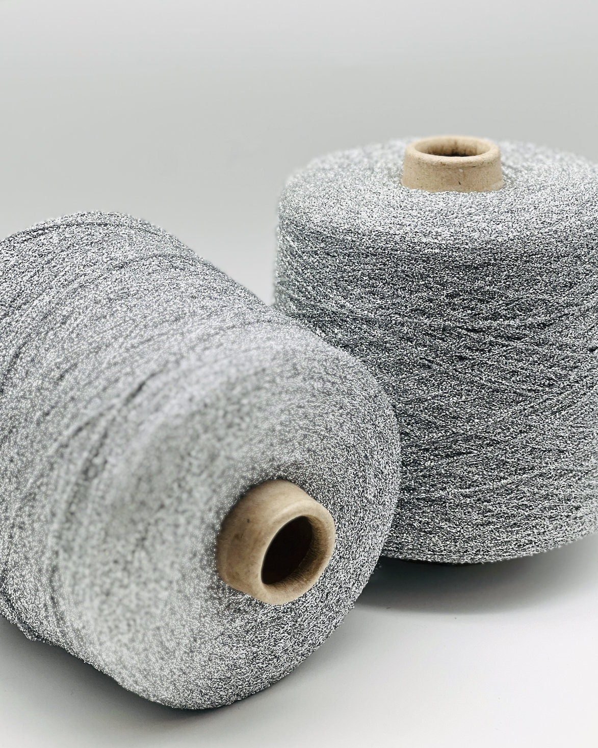 Two spools of silver yarn on a light gray background