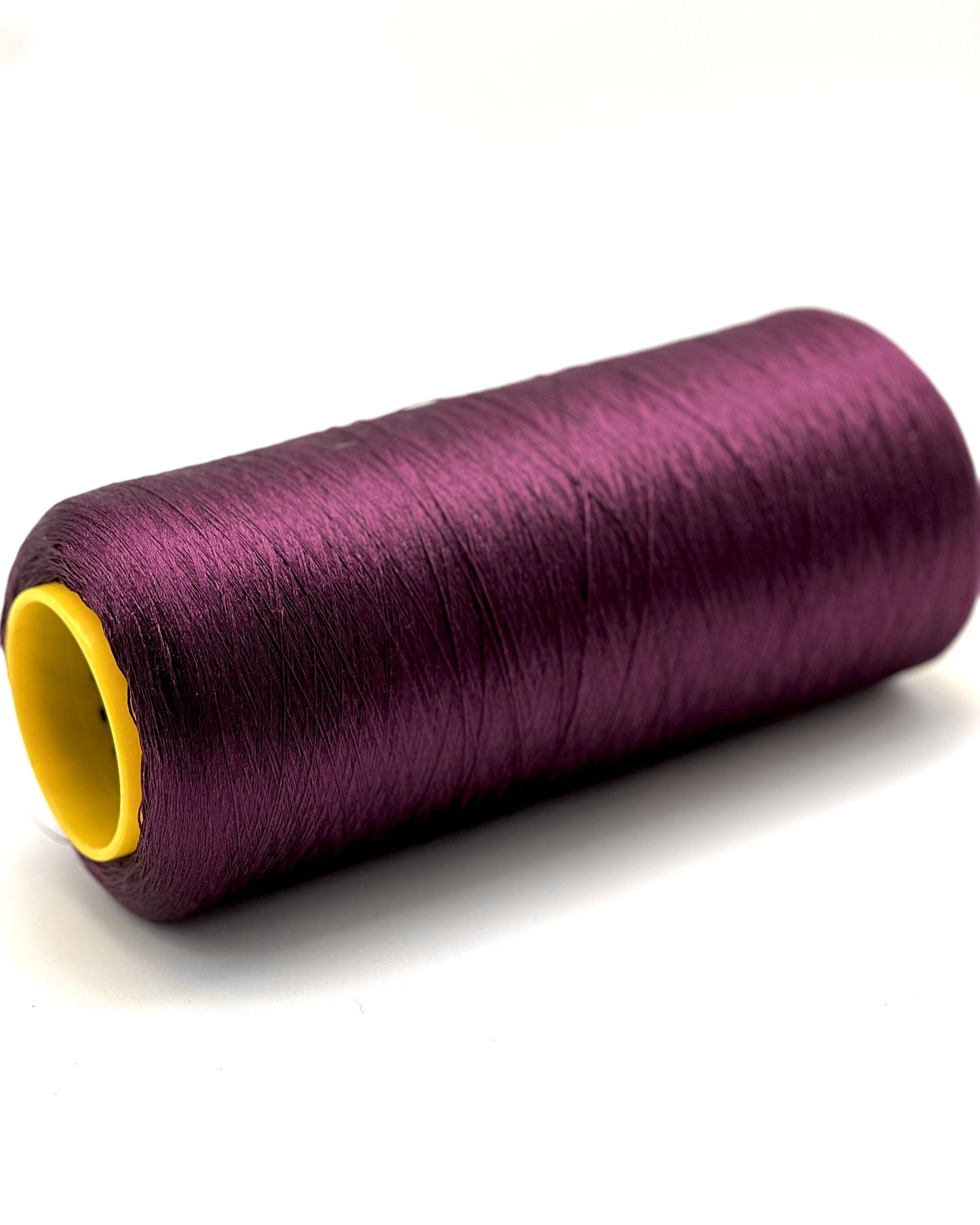 Purple spool of thread with a yellow core on a white background