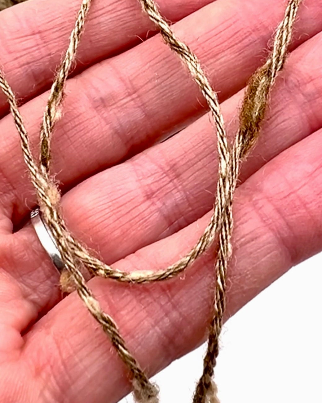Hand holding a piece of braided twine against a blurred natural background