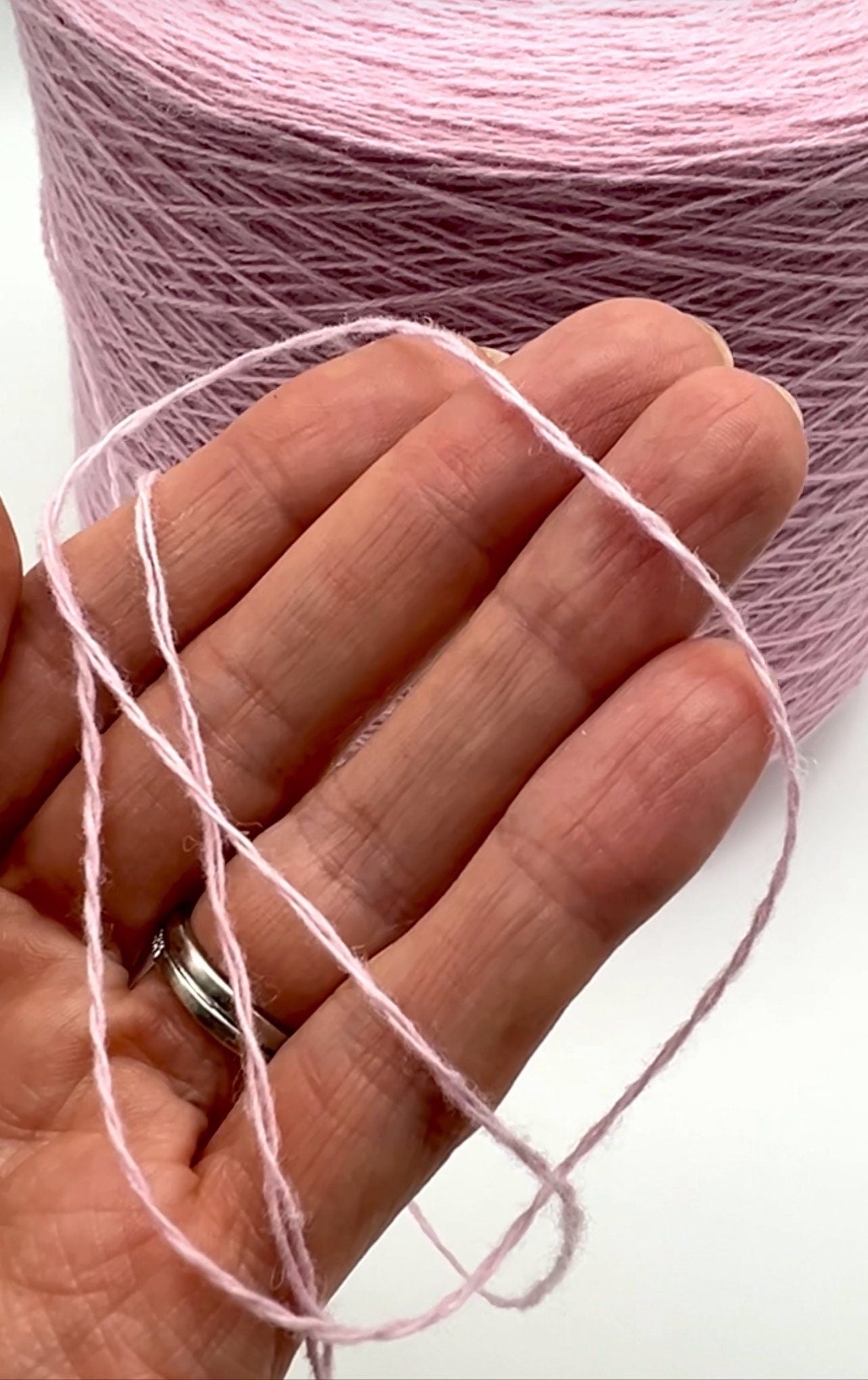 Close-up of pink yarn being held with a hand, with a ball of yarn in the background.