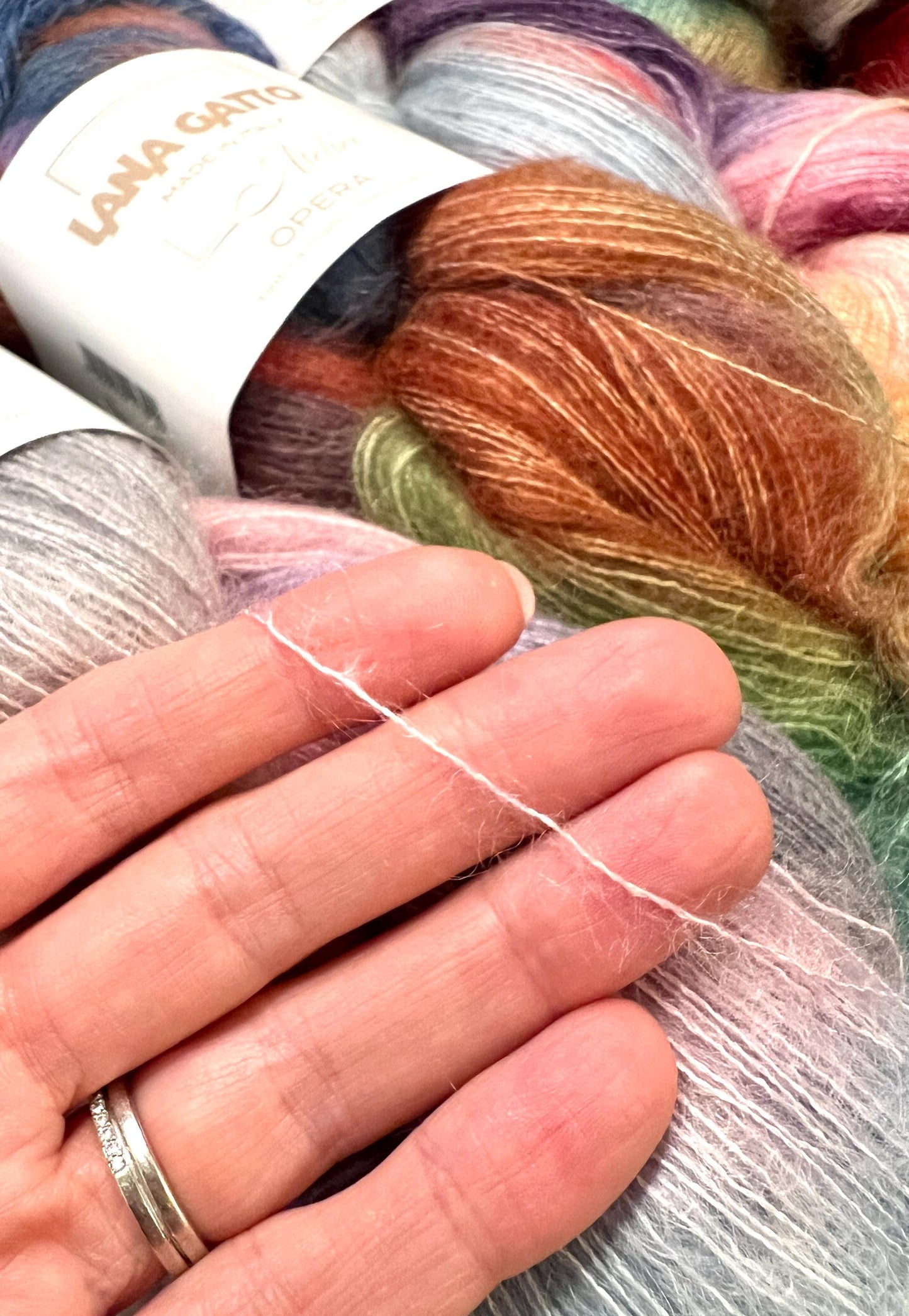 Close-up of colorful yarn with a hand holding a strand, LANA GARTEN branding visible.