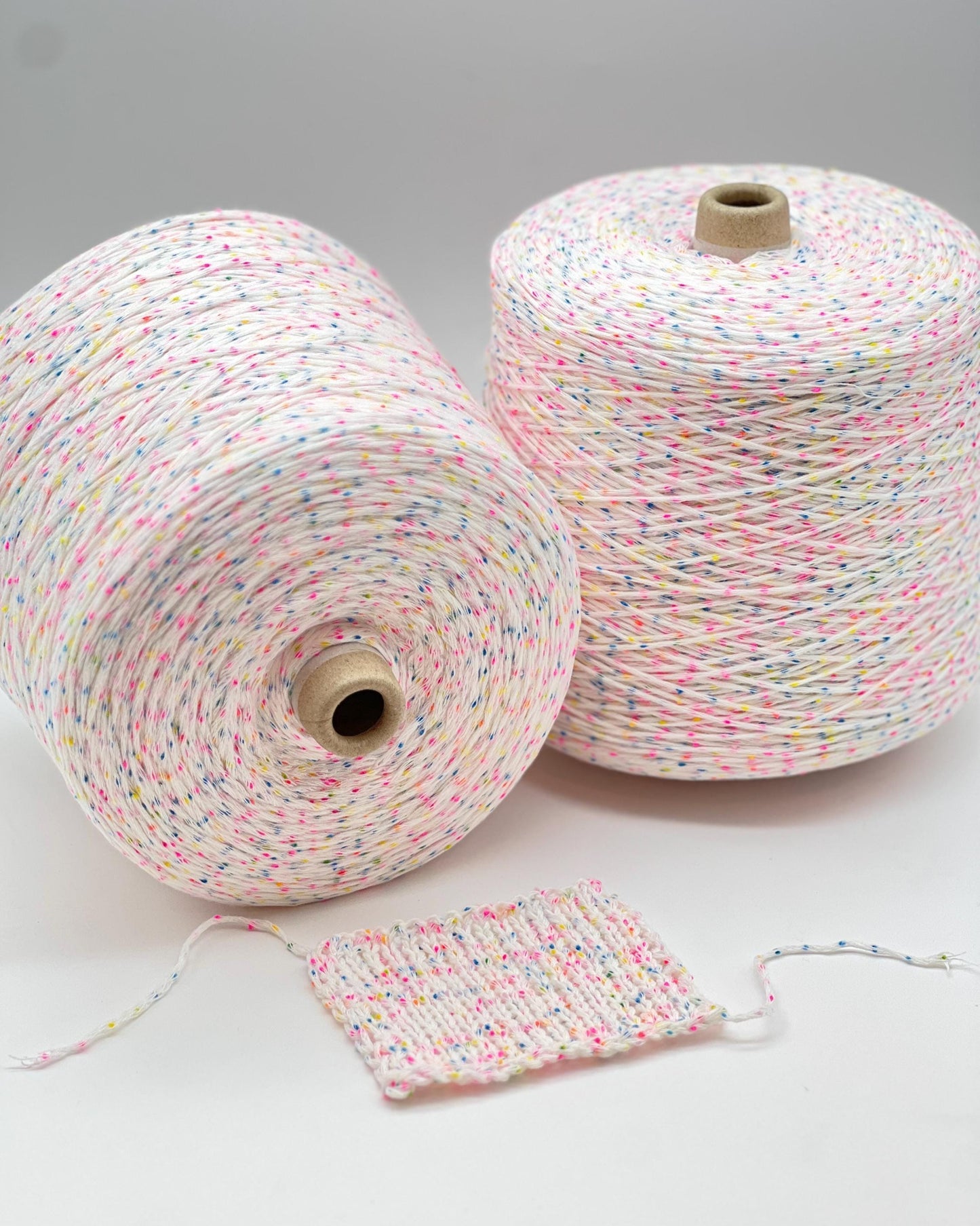 Two spools of multicolored yarn with a small swatch on a light gray background