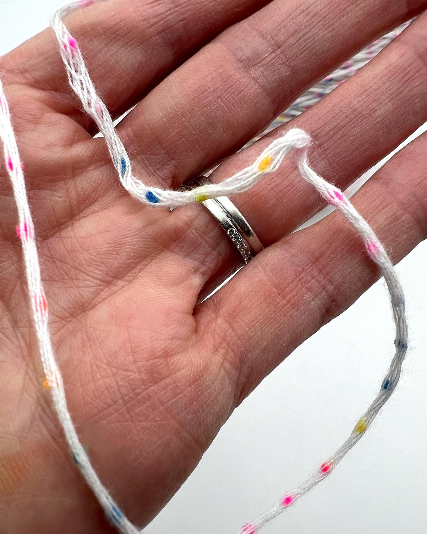 Hand holding a piece of string with colorful beads against a neutral background