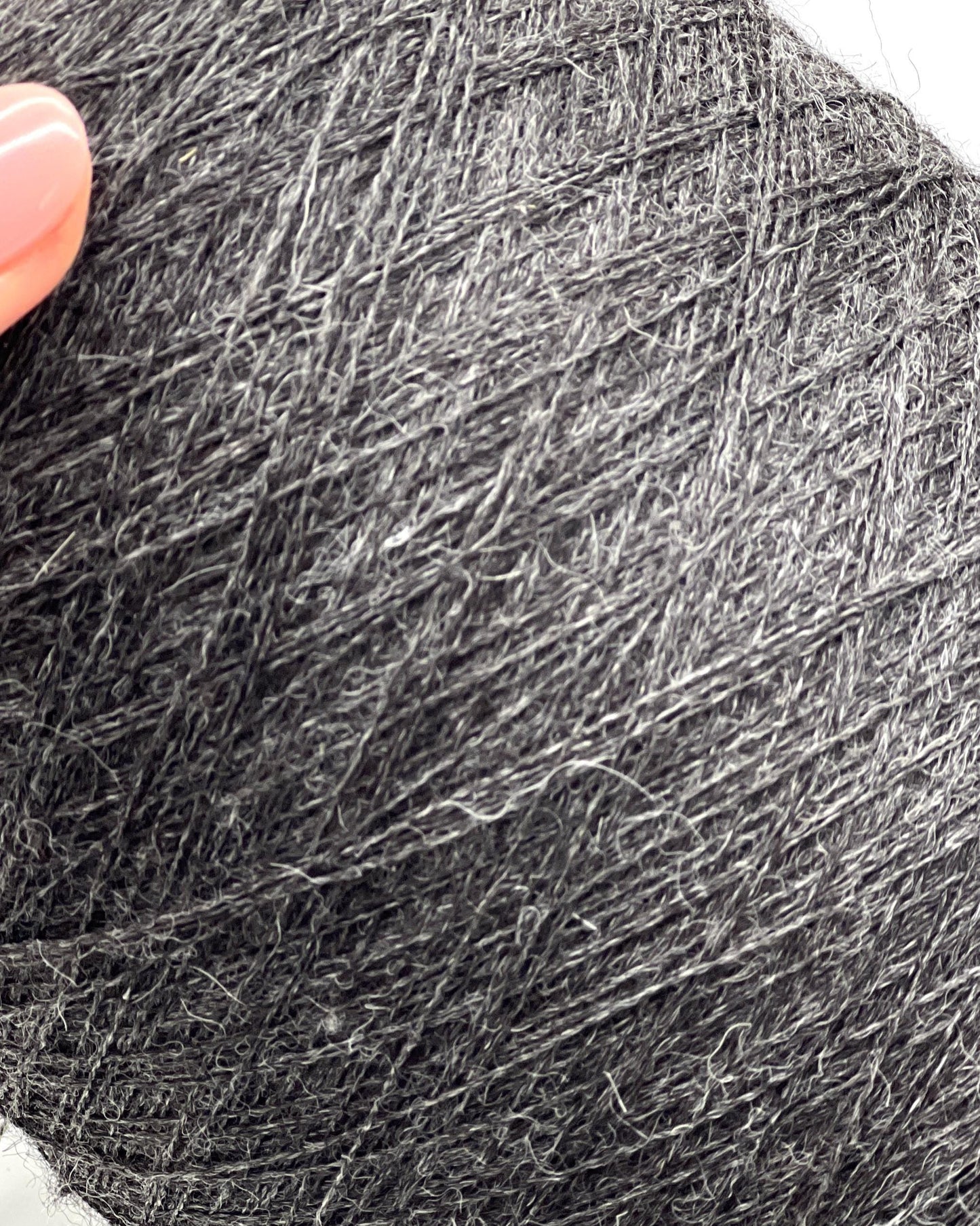 Close-up of a ball of dark gray yarn with a hand holding it.