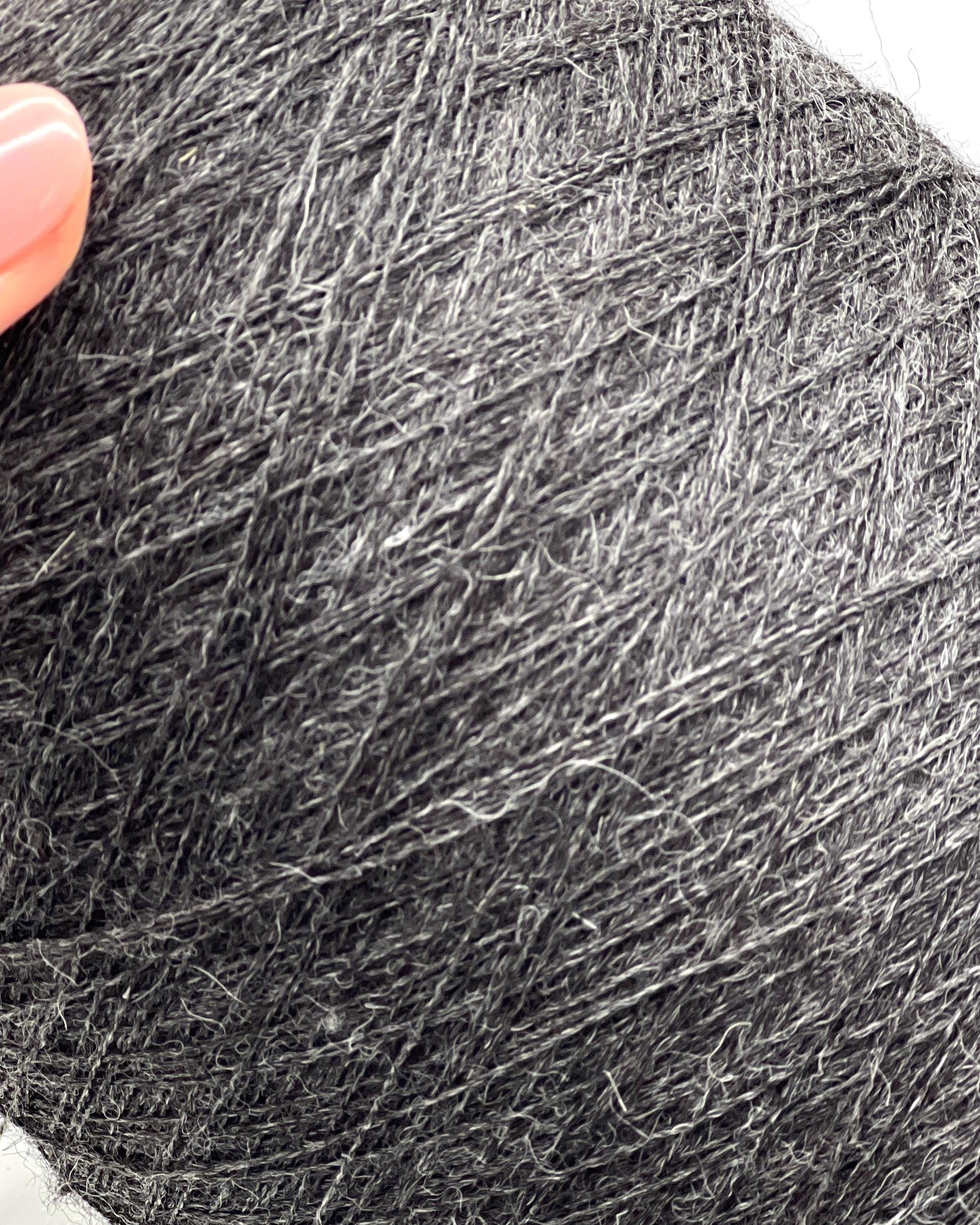 Close-up of a ball of dark gray yarn with a hand holding it.