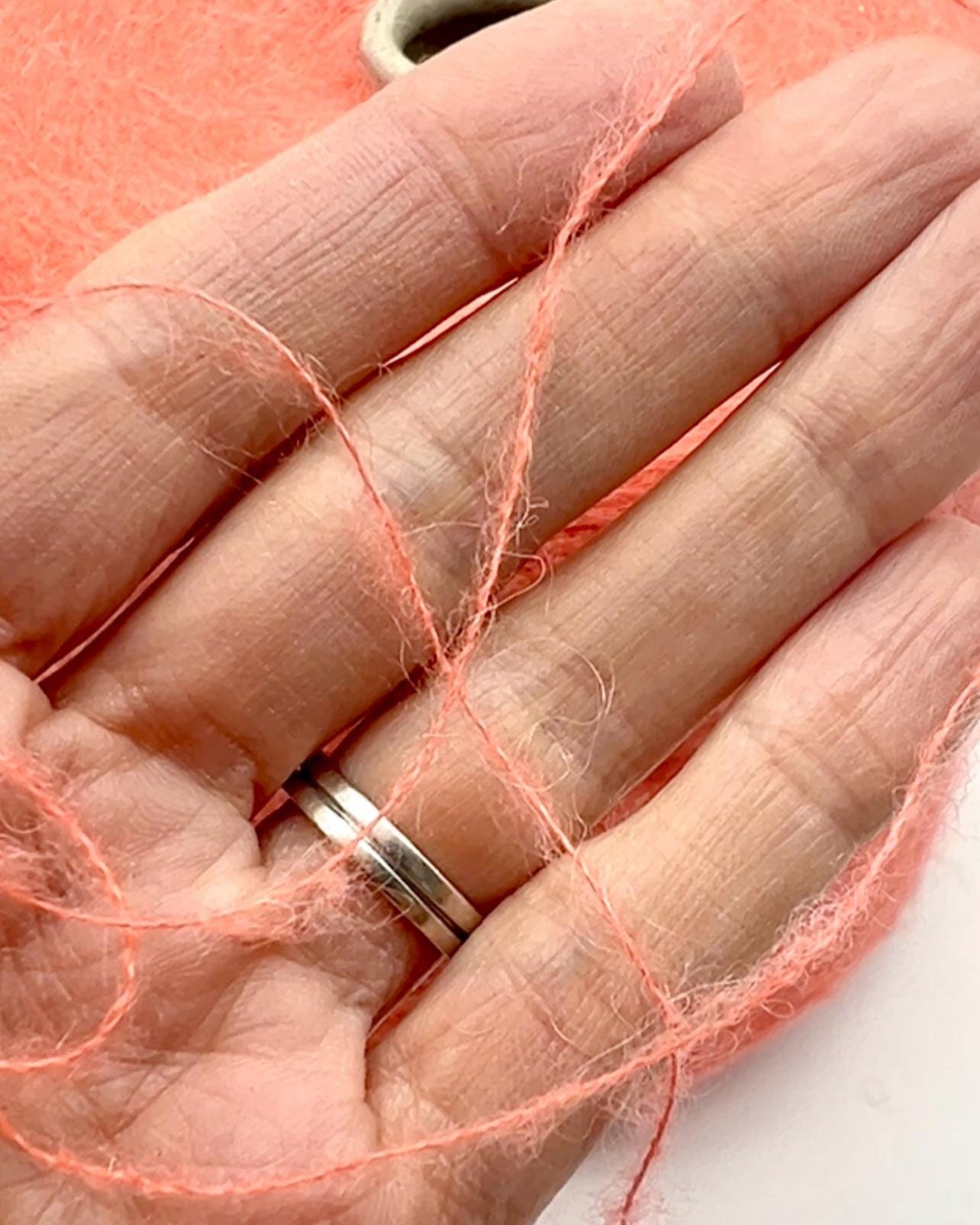 Hand wearing a silver ring with pink thread wrapped around it on a white background