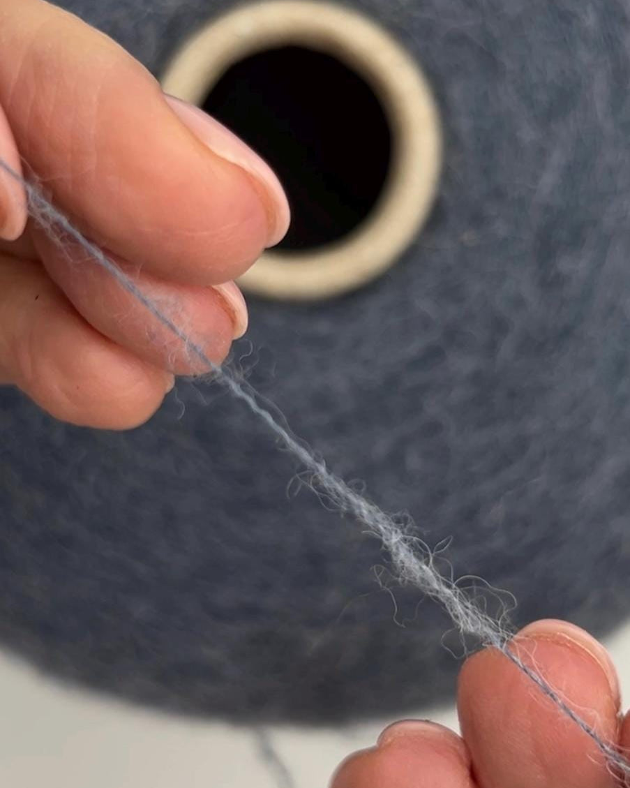 Close-up of hands holding gray yarn with a blue spool in the background